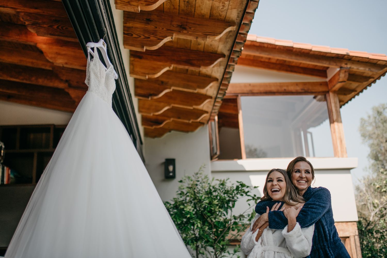 Couple stands on porch near white teepee structure in outdoor setting at sunset.