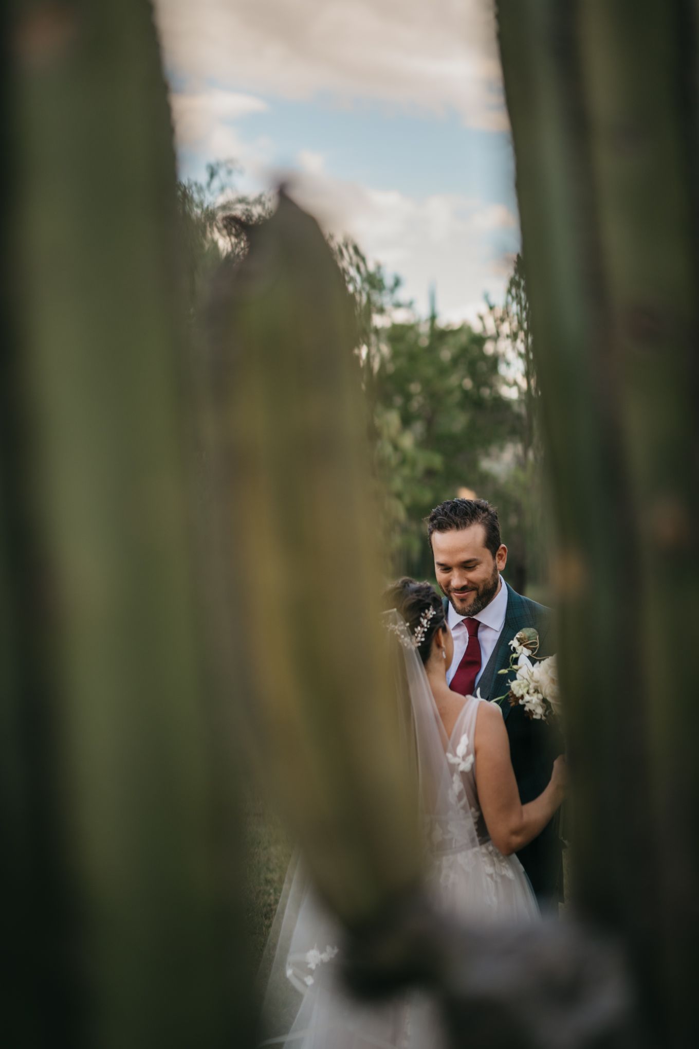 Creative wedding photography shot through greenery during an outdoor ceremony.
