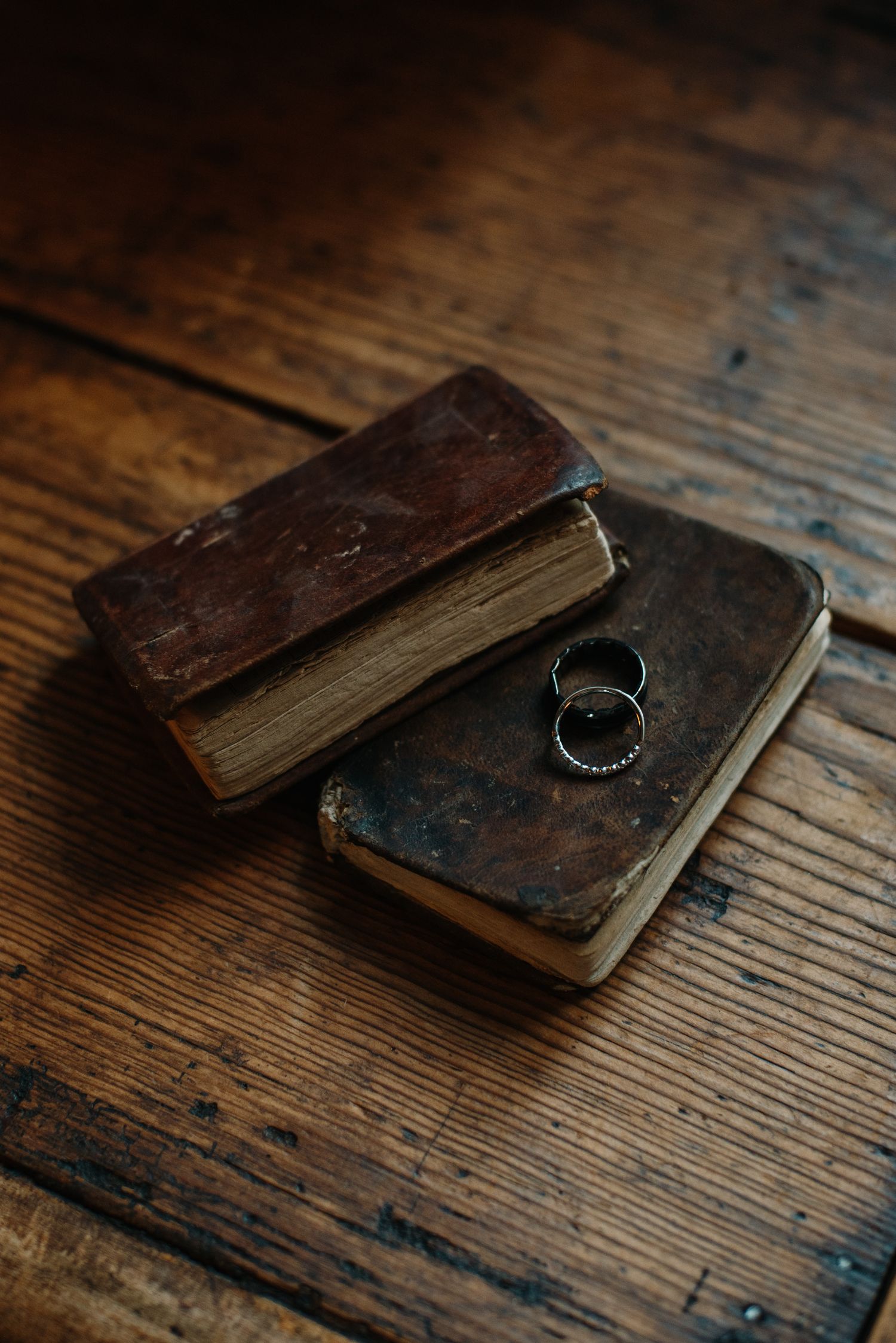 Wedding rings resting on vintage leather-bound books on wooden surface.
