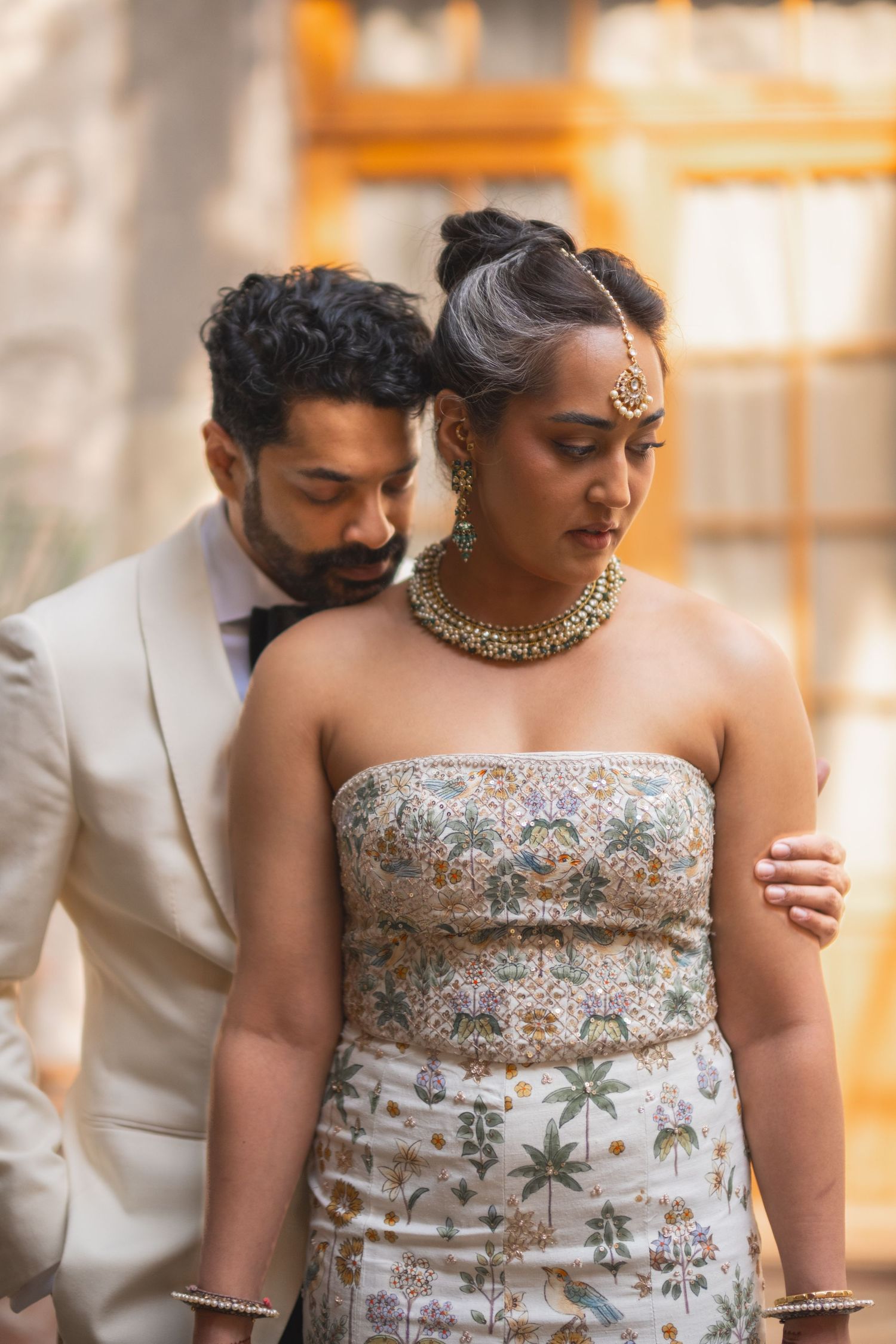 Intimate wedding portrait featuring ornate Indian bridal jewelry and a white formal suit.