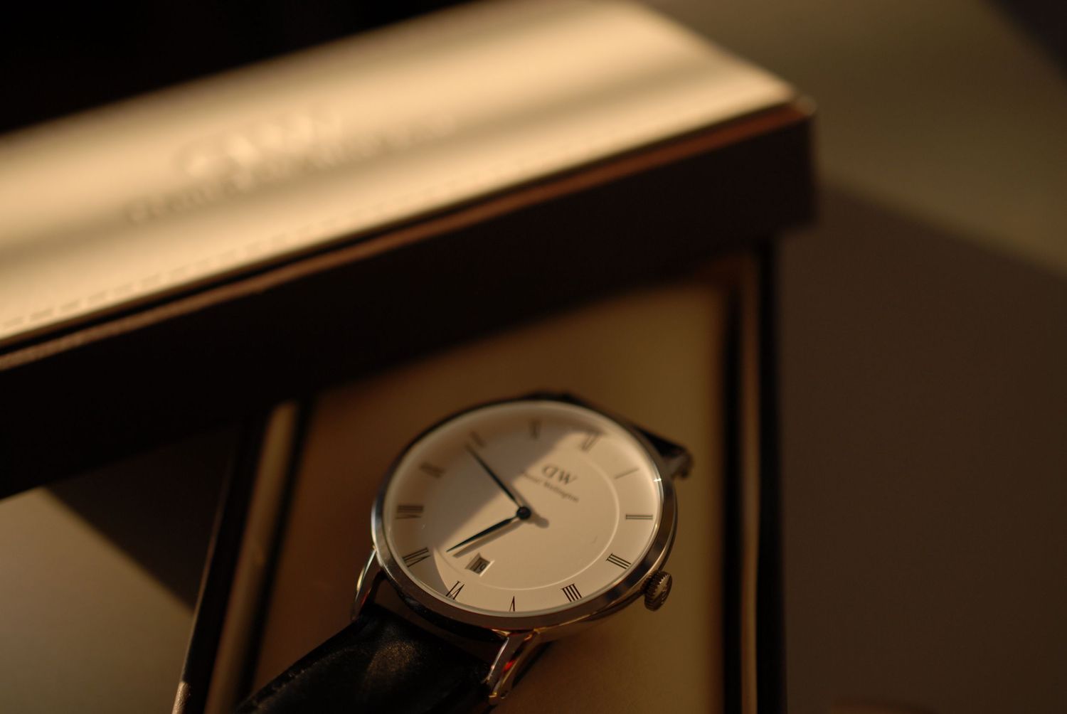 Elegant wristwatch with leather strap on dark wooden surface in ambient lighting.