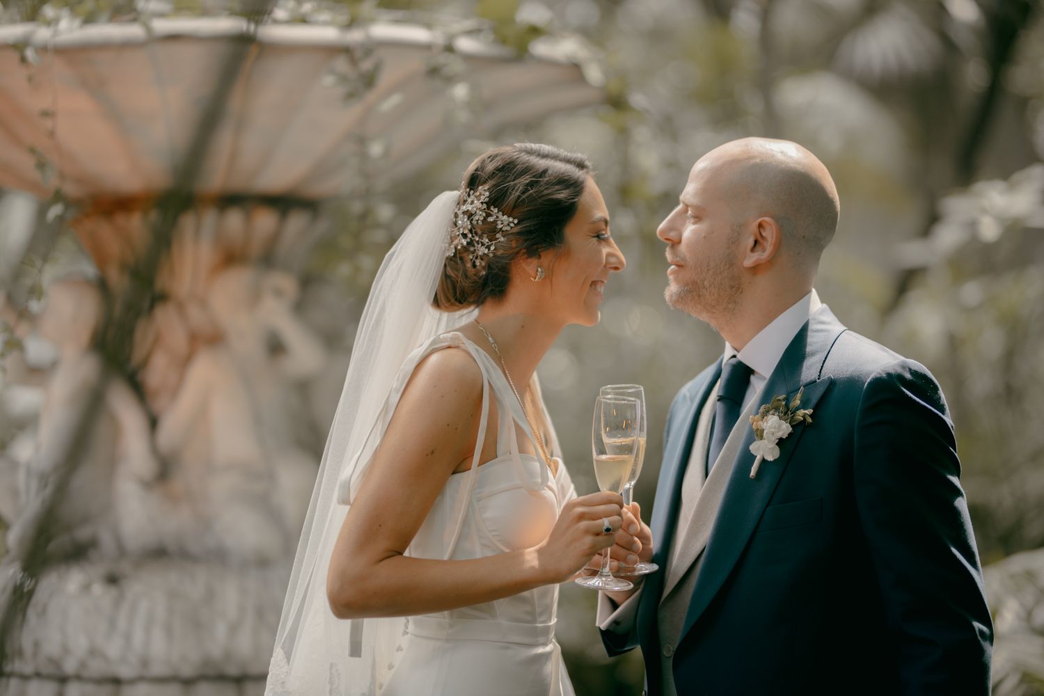 A romantic wedding moment captured outdoors with champagne glasses and soft natural lighting.