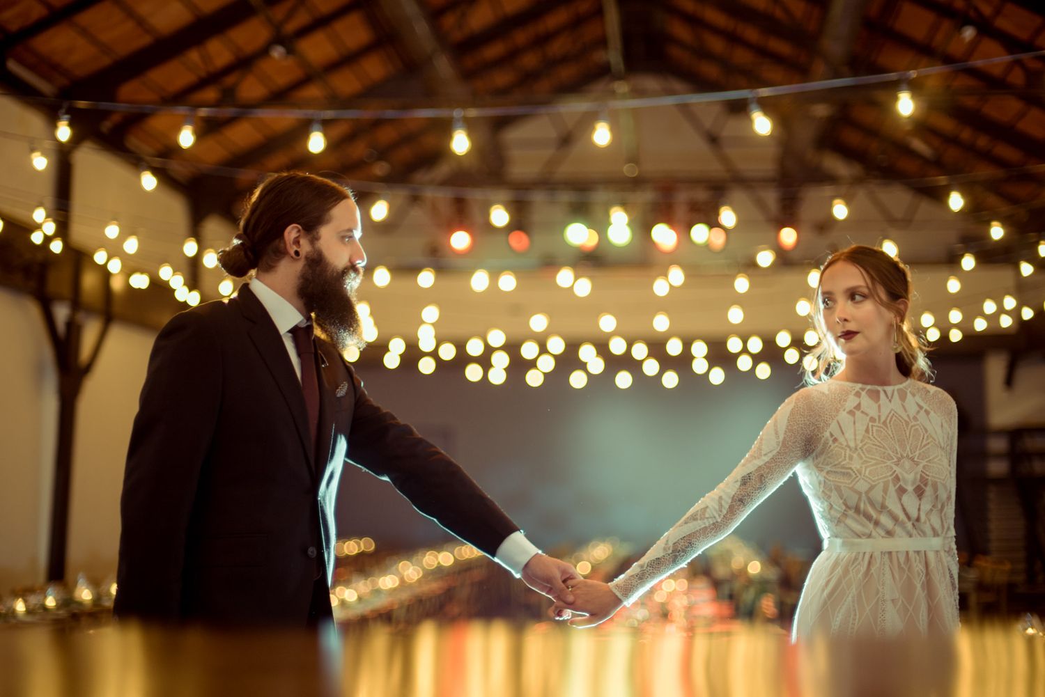 A romantic couple dances in a rustic venue decorated with warm glowing string lights on the ceiling.