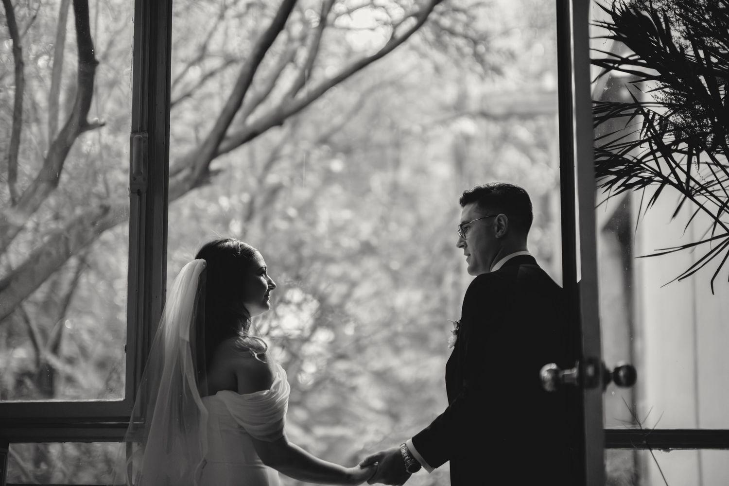 Black and white wedding photo capturing couple by window.