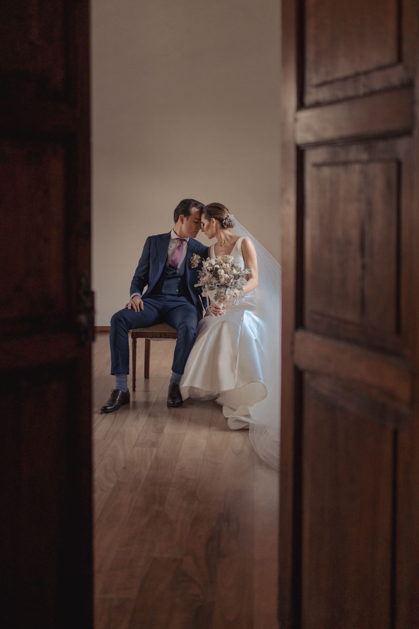 Intimate moment between newlyweds seated in wooden doorway.