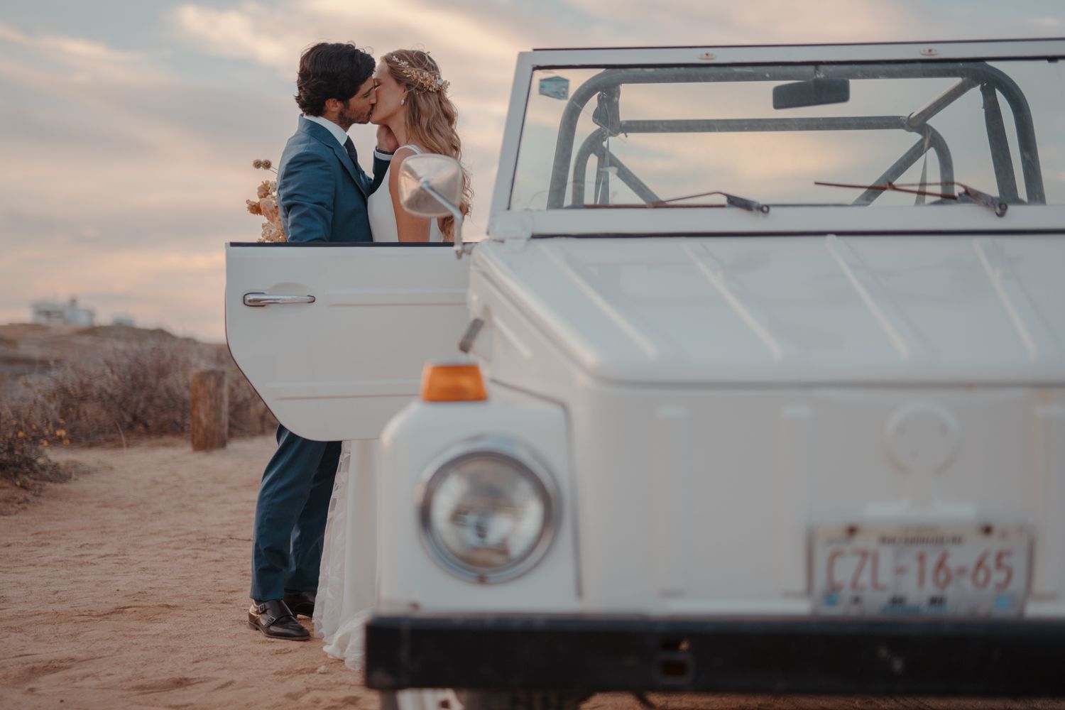 A romantic moment beside a vintage white vehicle during a sunset wedding photoshoot.