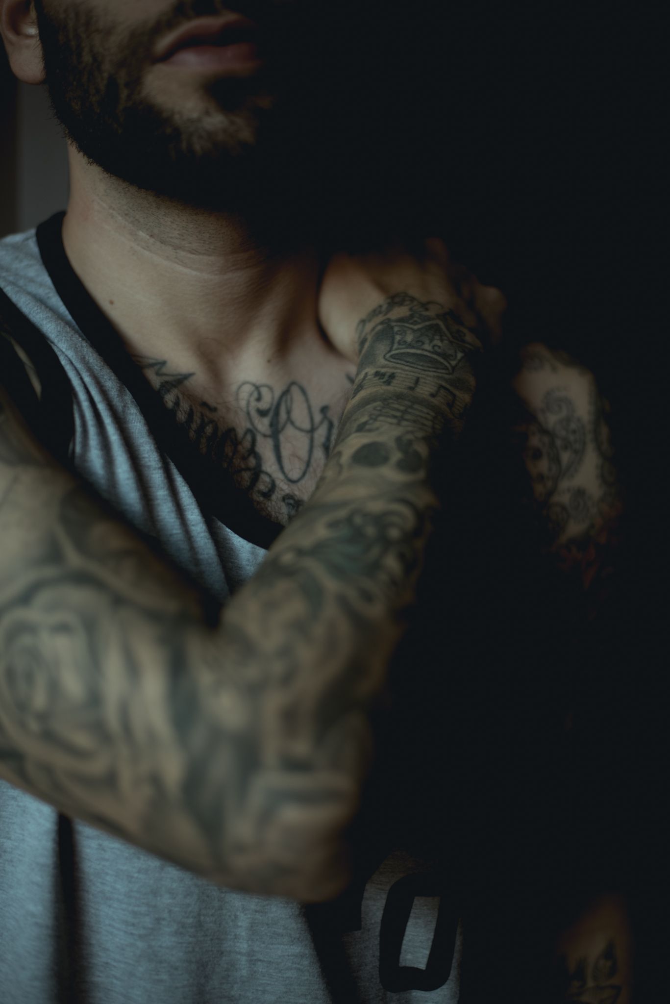 Dramatic lighting highlights intricate tattoo work and grey athletic tank top design.