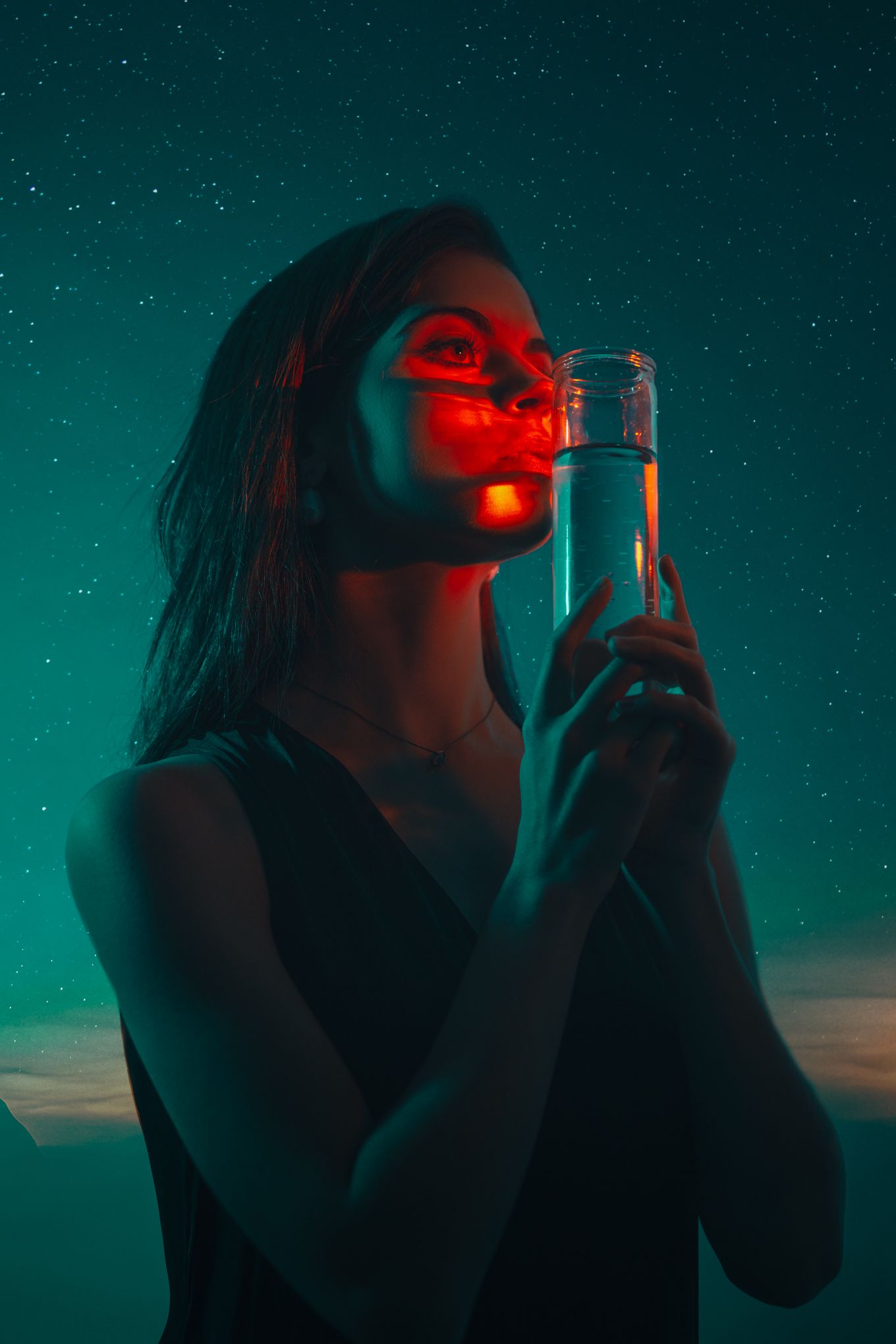 Moody portrait with bottle against starry teal sky and red lighting.