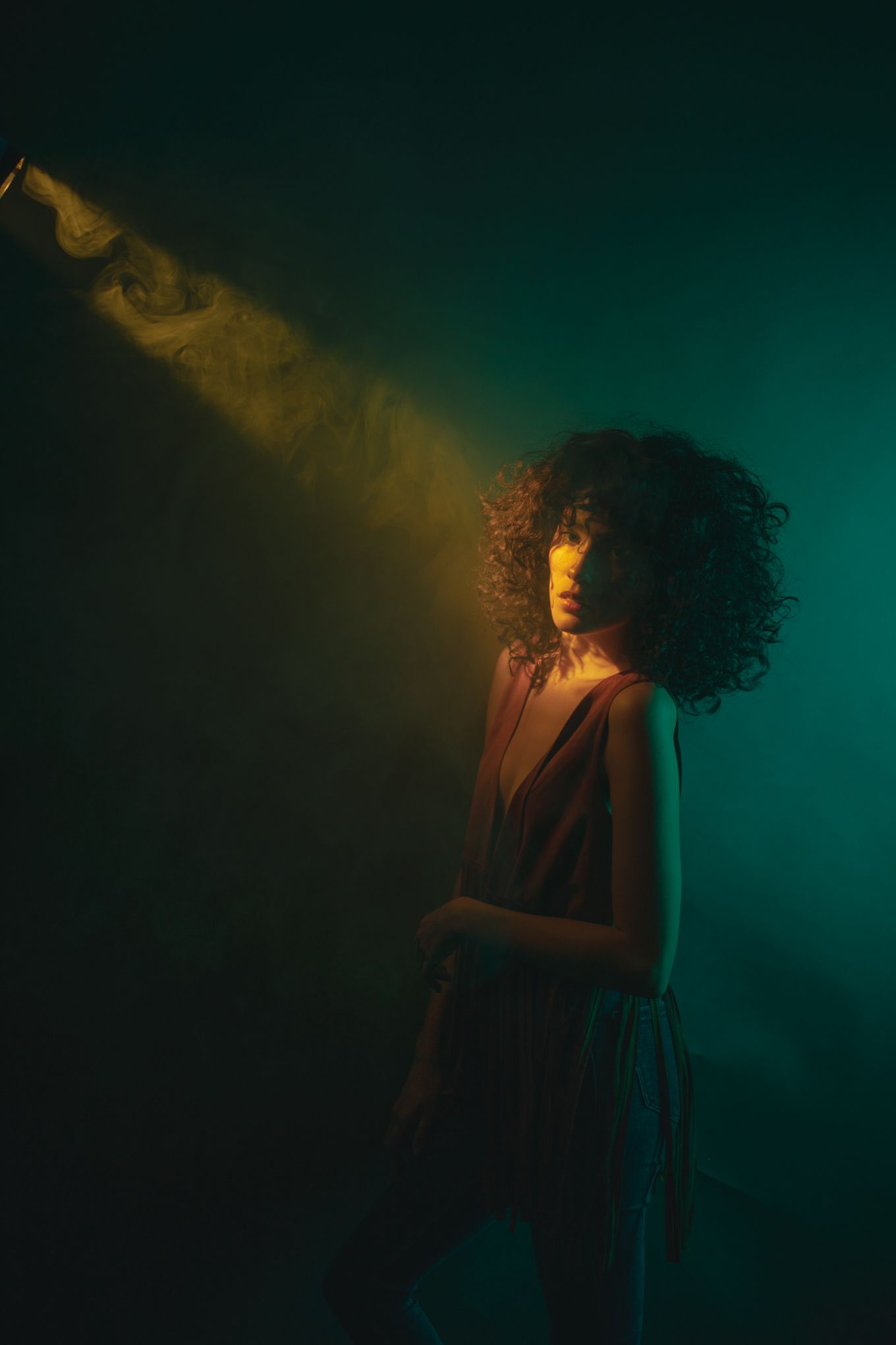 Dramatic portrait in dark moody lighting with golden beam illuminating figure against emerald backdrop.