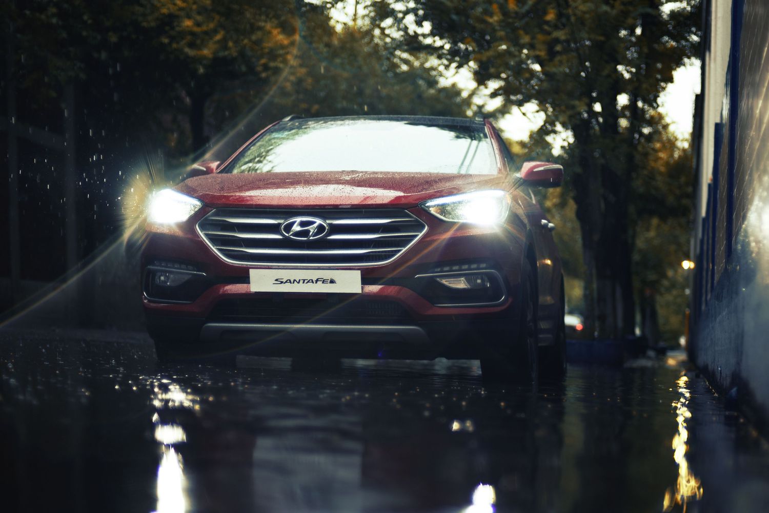 A modern black Hyundai SUV drives on a tree-lined road at dusk with headlights illuminating the path ahead.