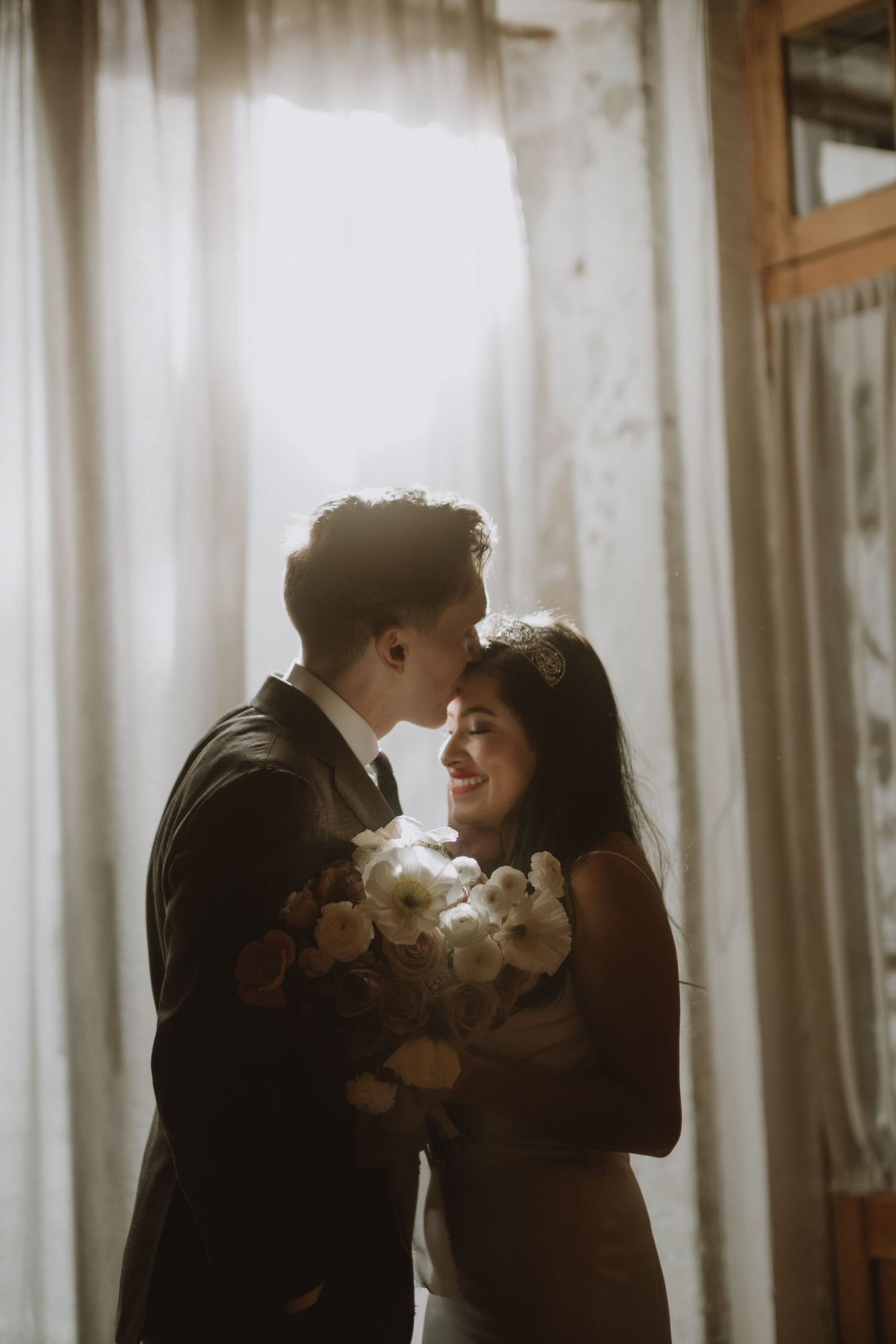 Intimate wedding portrait silhouetted against bright window light.