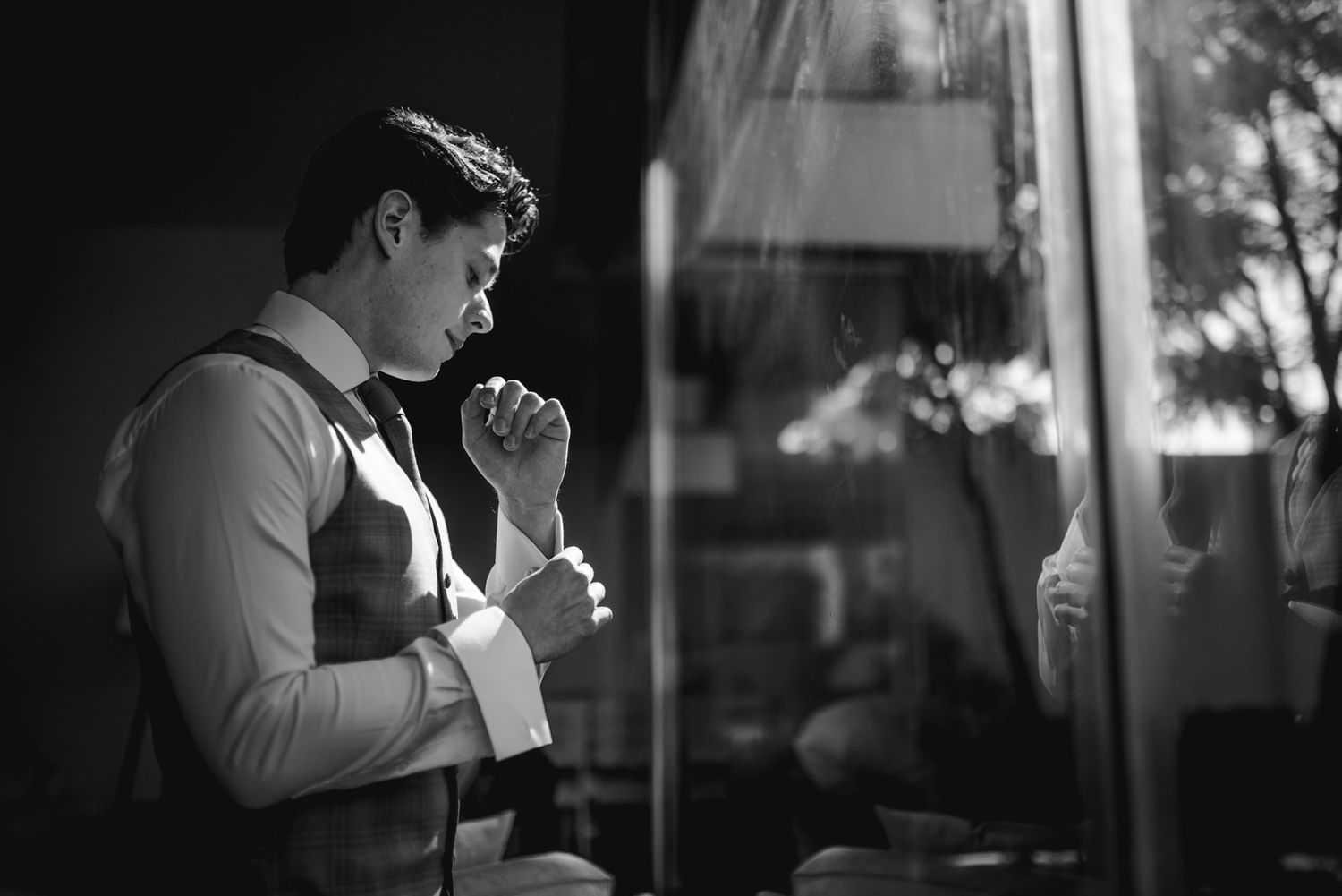 Person in vest standing by window in dramatic black and white composition.