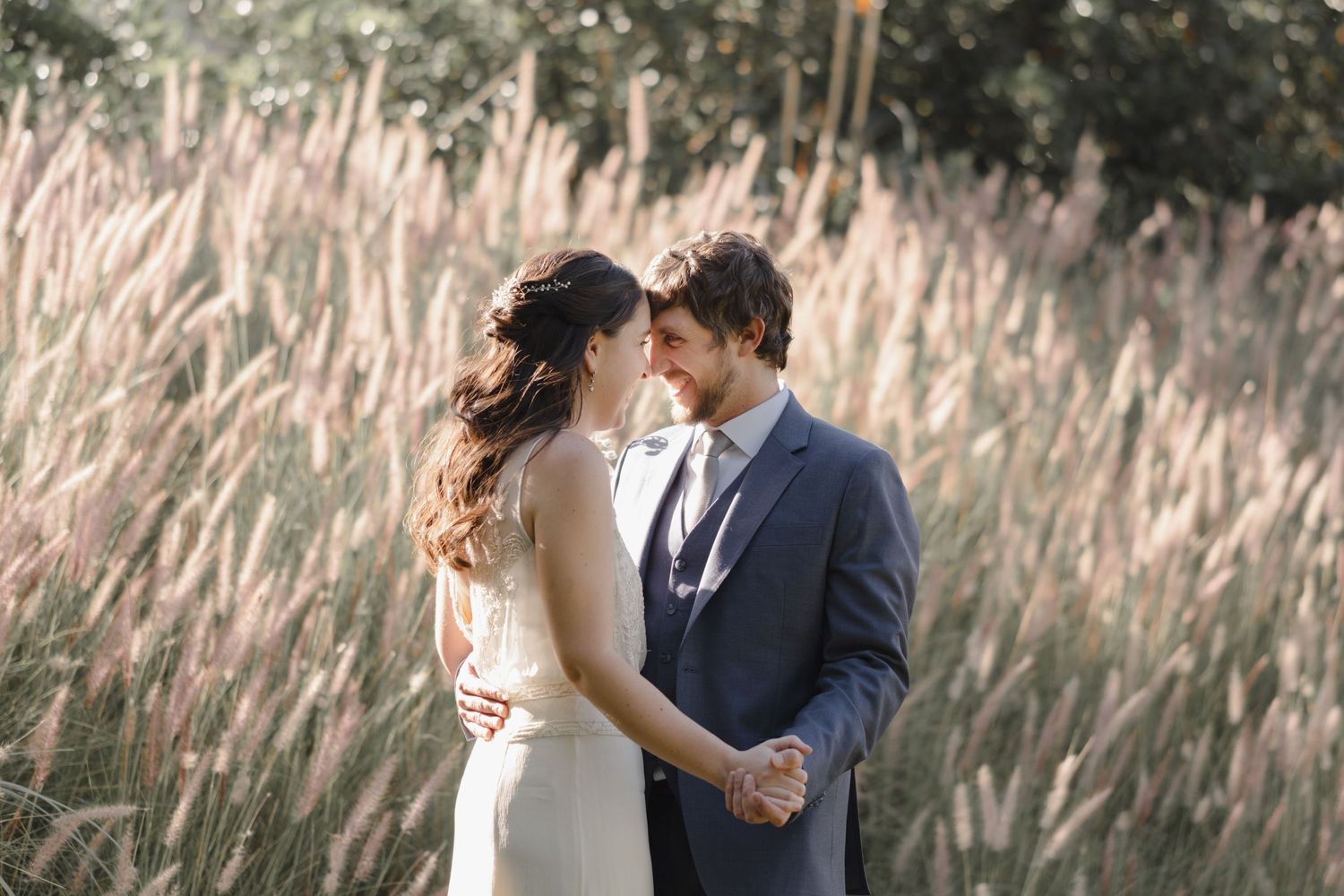 Romantic wedding portrait of couple embracing in field of tall grasses at sunset.