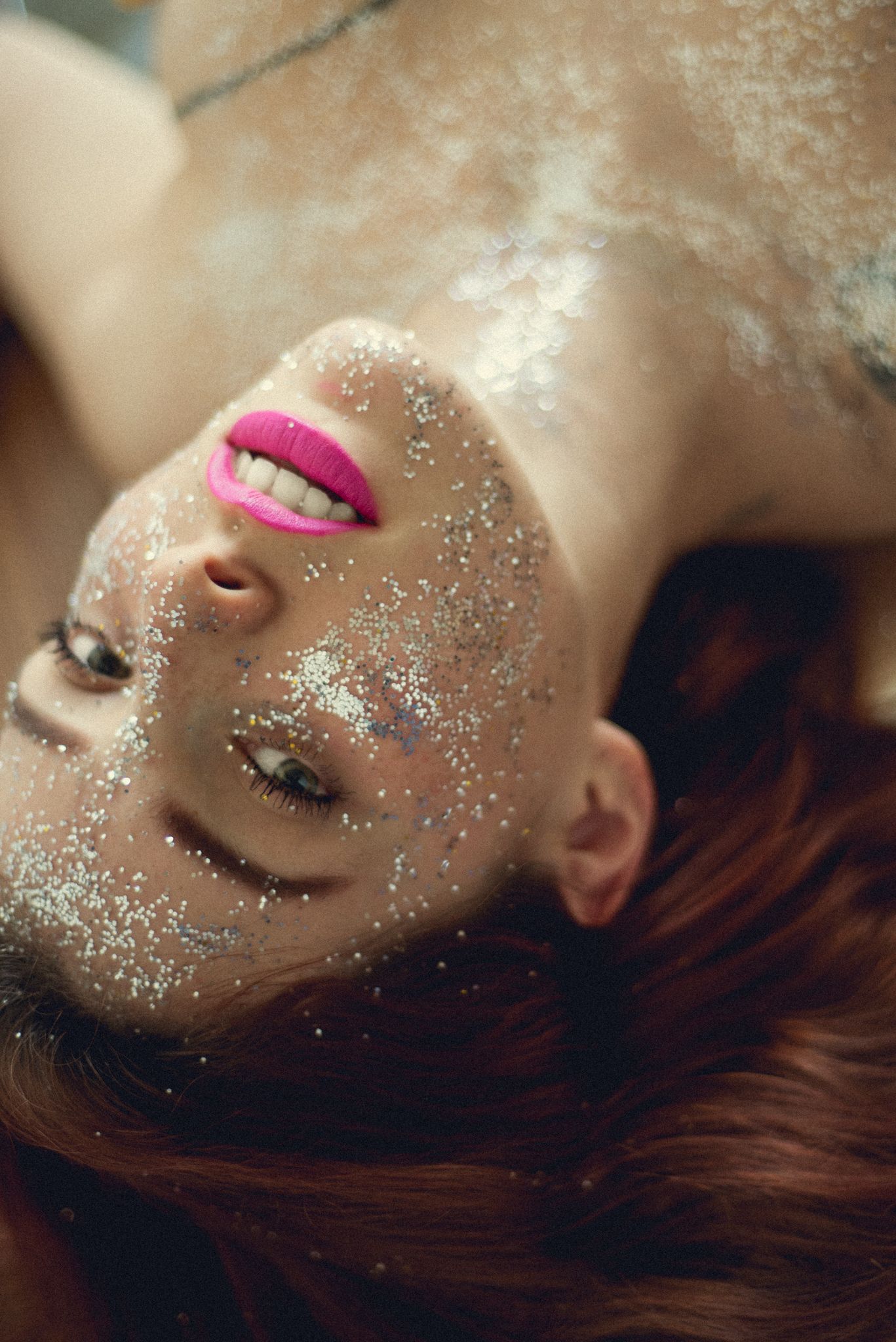 Dreamy portrait with bright pink lipstick and glitter-covered skin in soft lighting.