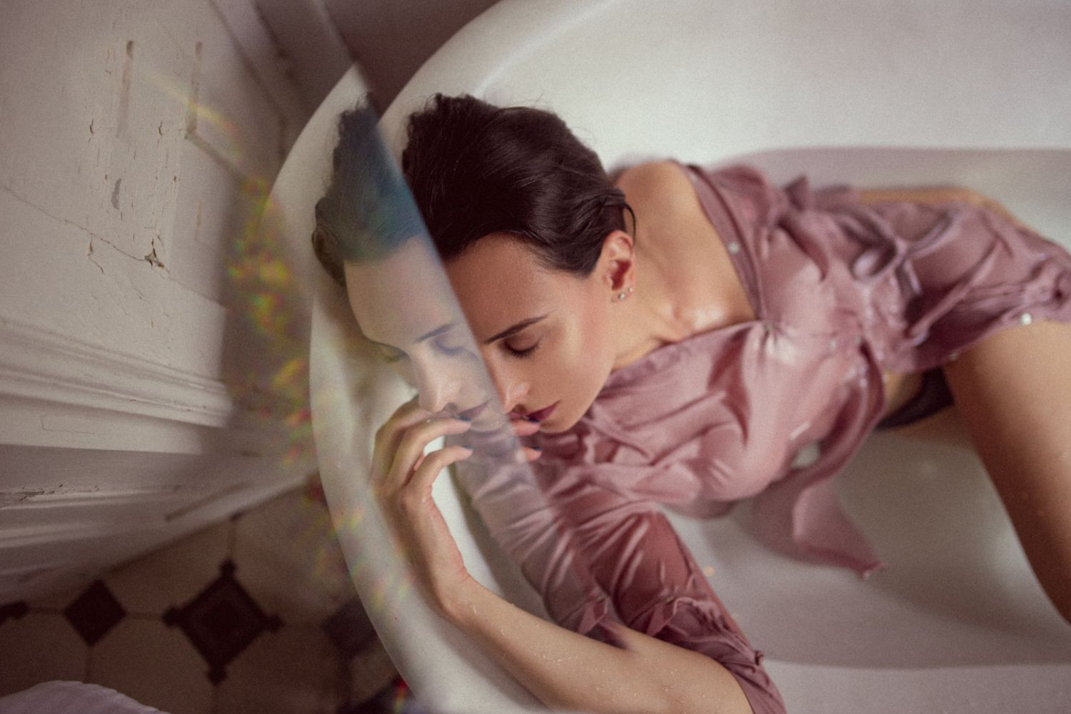 Artistic portrait in pink dress reclining in white bathtub.