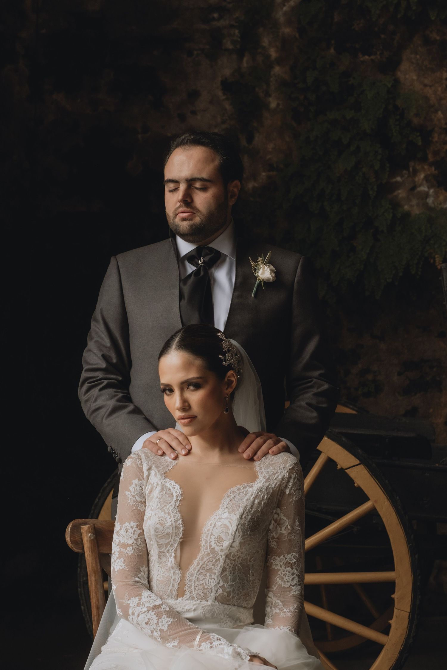 Classic wedding portrait with couple posed against rustic backdrop with wooden wheel.