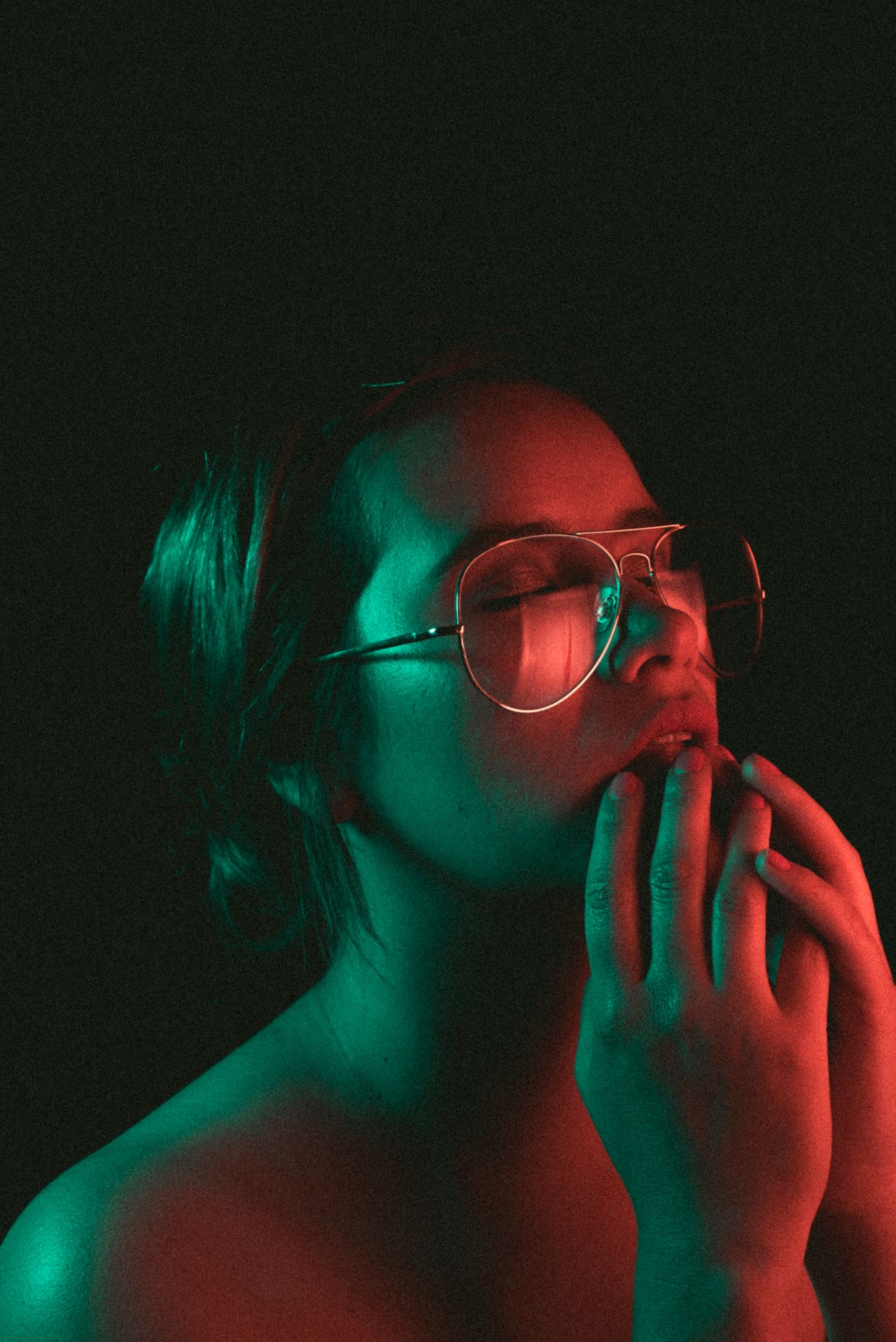 Portrait with glasses in neon red and green lighting against dark background.