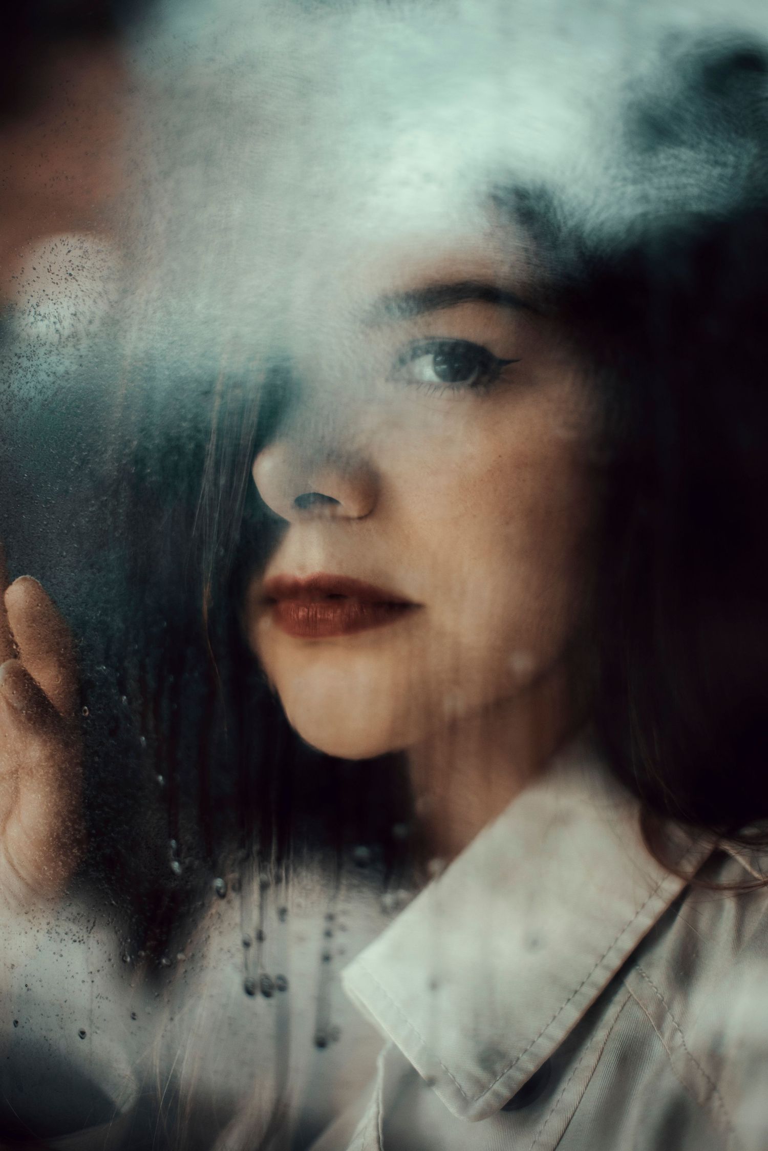 Close-up portrait through misty glass with dramatic lighting and red lipstick.