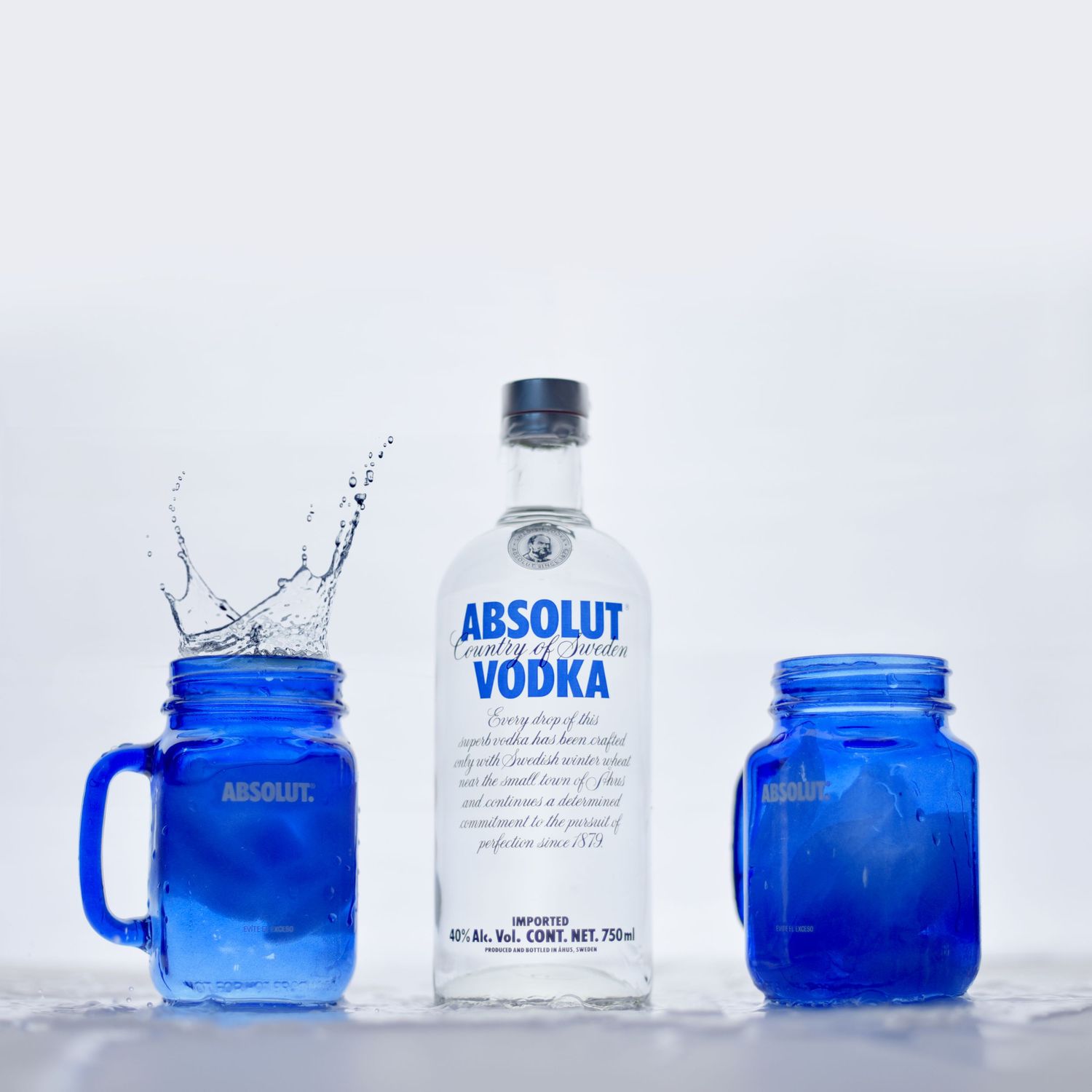 Blue glass jars and a bottle of Absolut vodka arranged artistically against a white backdrop in a minimalist composition.