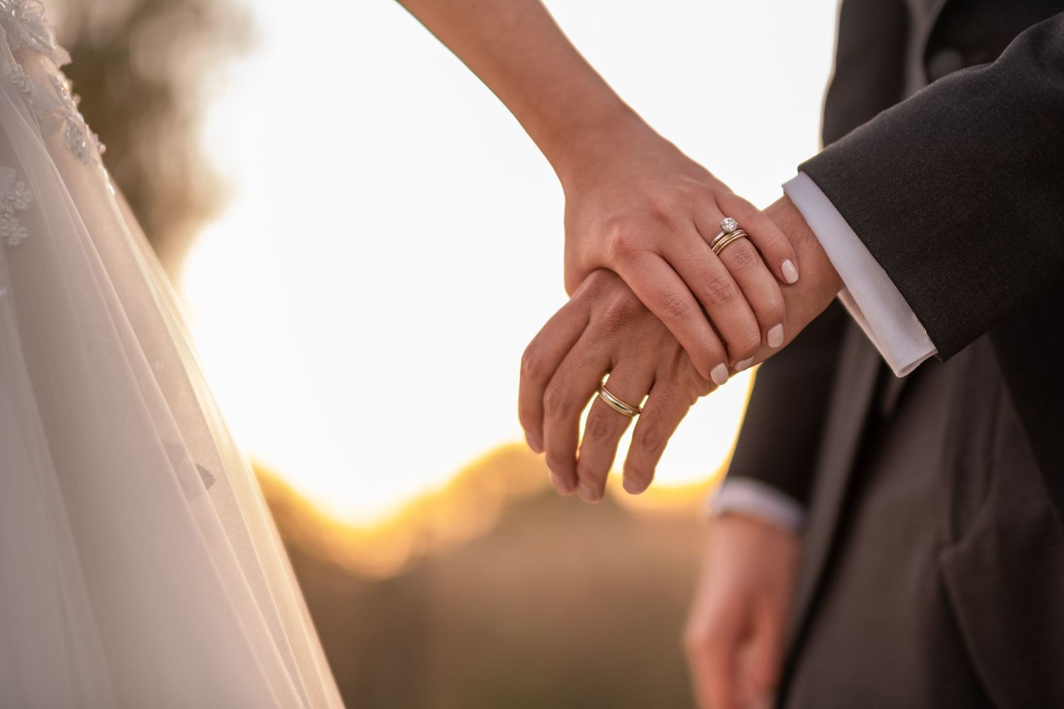 Newlywed couple holding hands showing wedding rings during golden sunset.