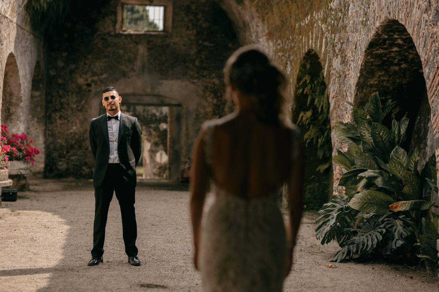 A couple shares their first look moment in a rustic stone courtyard with arches and lush greenery.