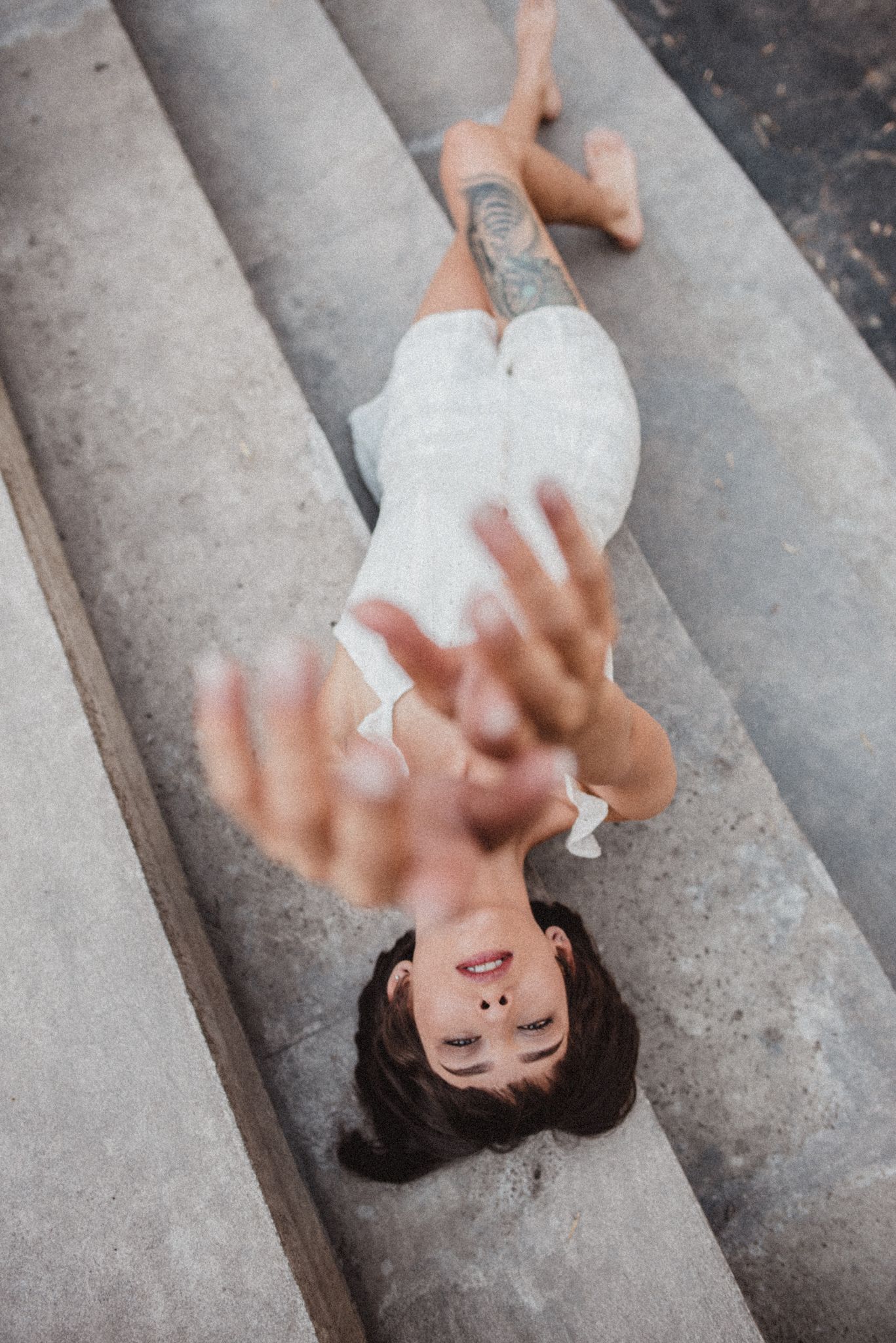 Artistic overhead shot of woman in white dress lying on concrete steps.