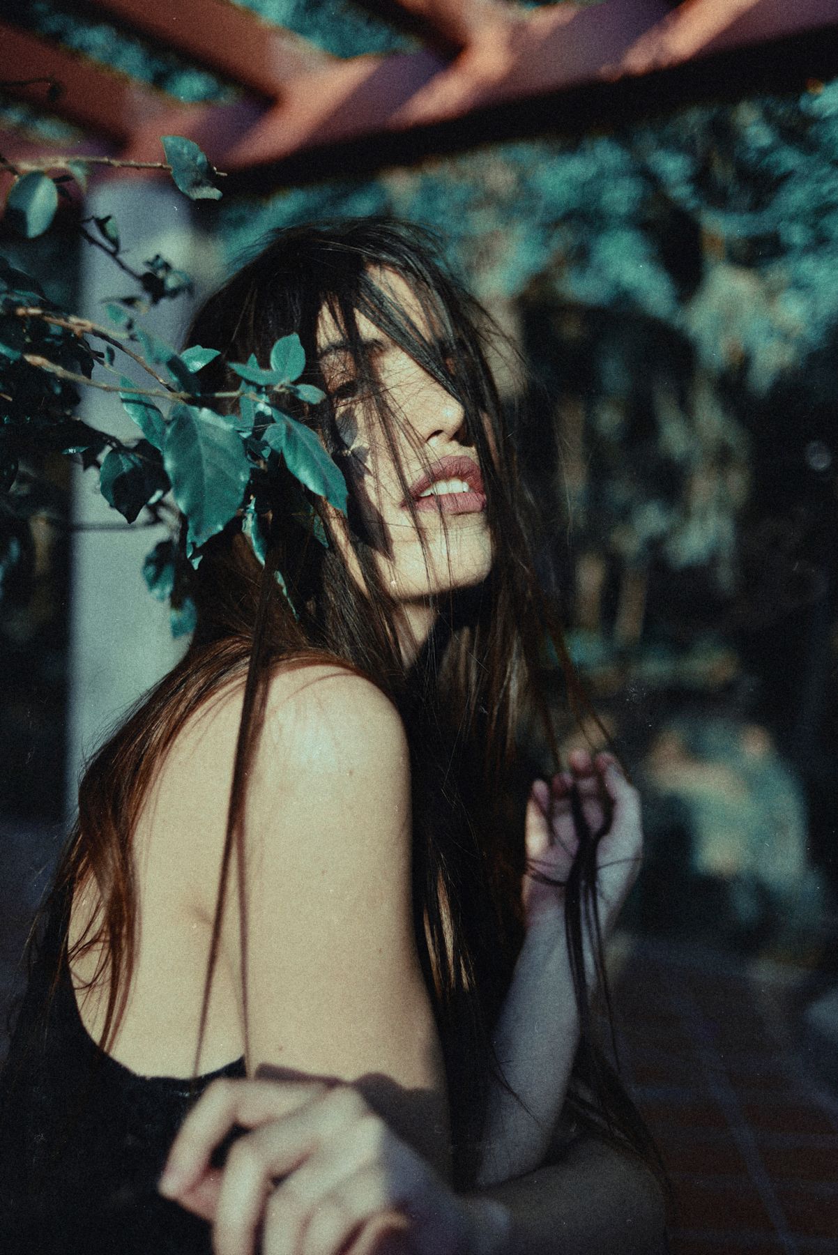 Atmospheric portrait with leaves framing dark-haired figure in black clothing.