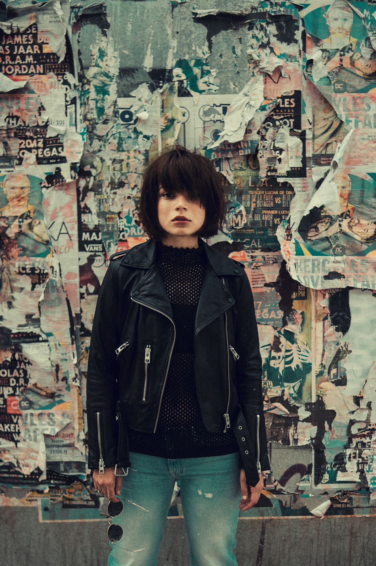 Edgy portrait against wall covered in torn posters and urban street art.