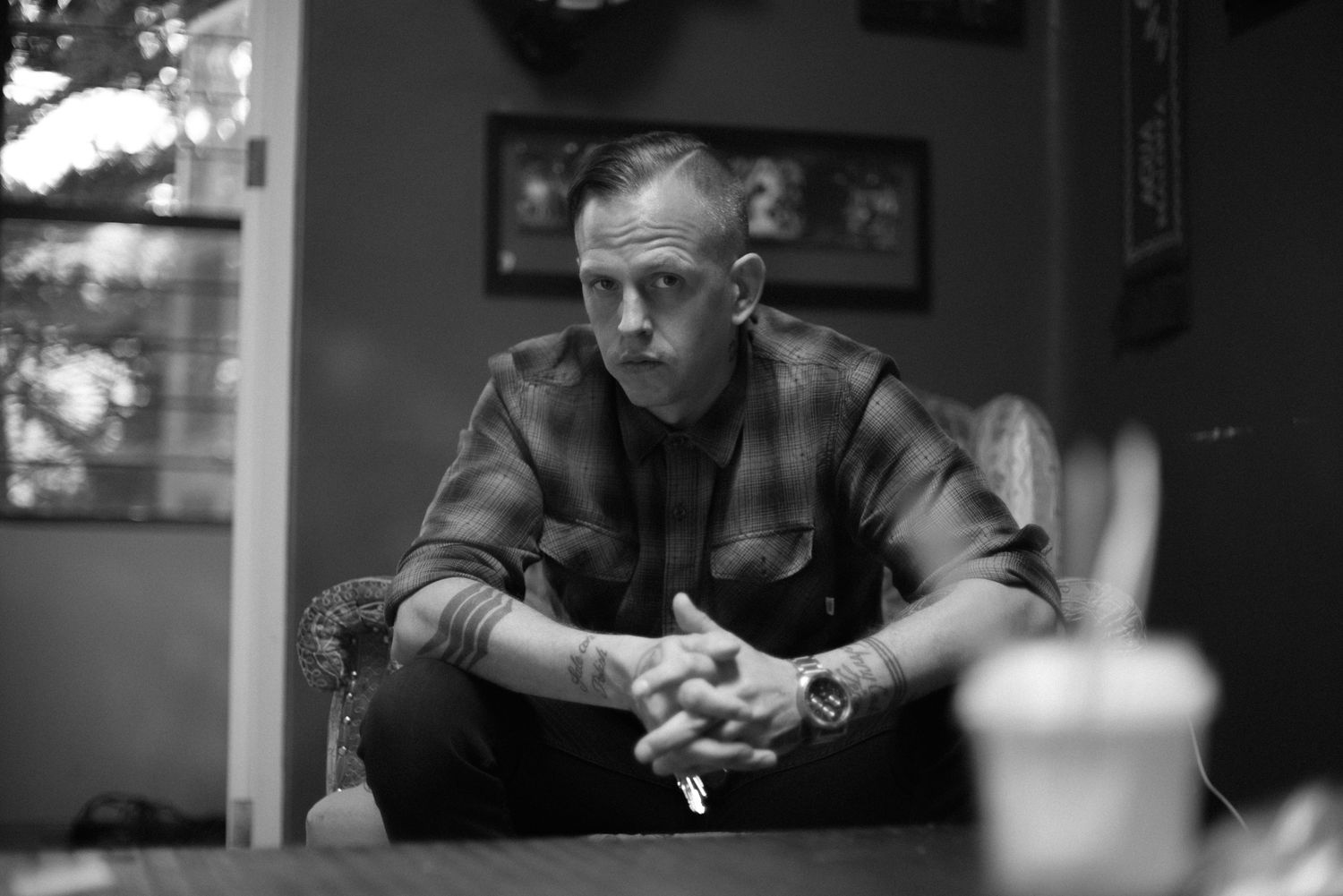 Black and white portrait of person sitting at table with drink in moody lighting.