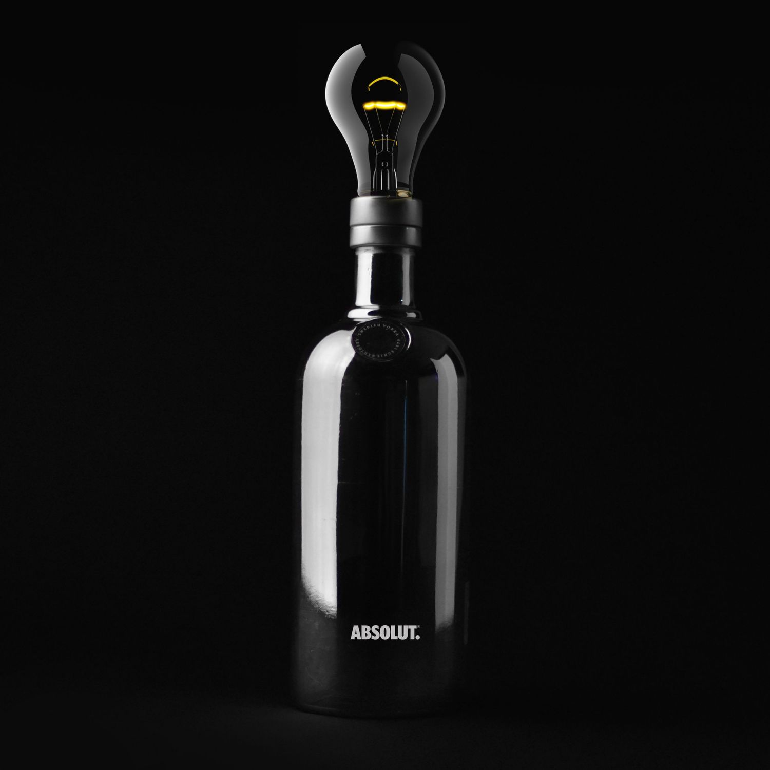 Black Absolut vodka bottle with light bulb stopper against dark background.