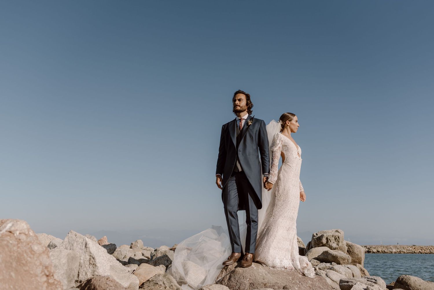 Seaside wedding photography with couple standing on rocky coastline.