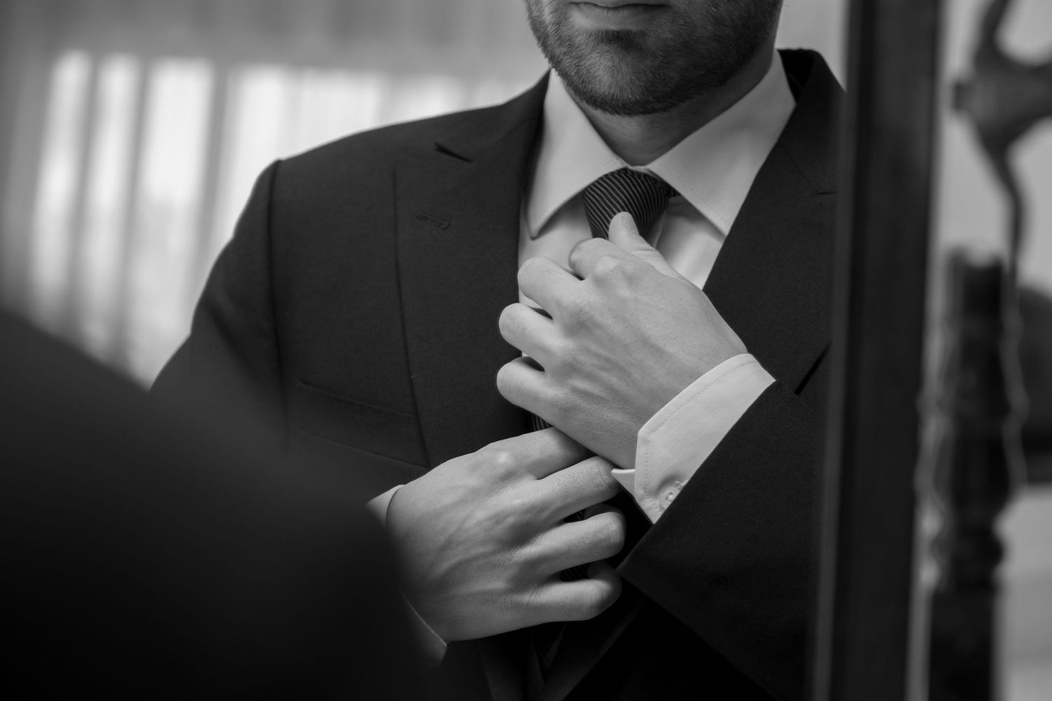 Close-up black and white shot of hands adjusting a formal suit and tie.