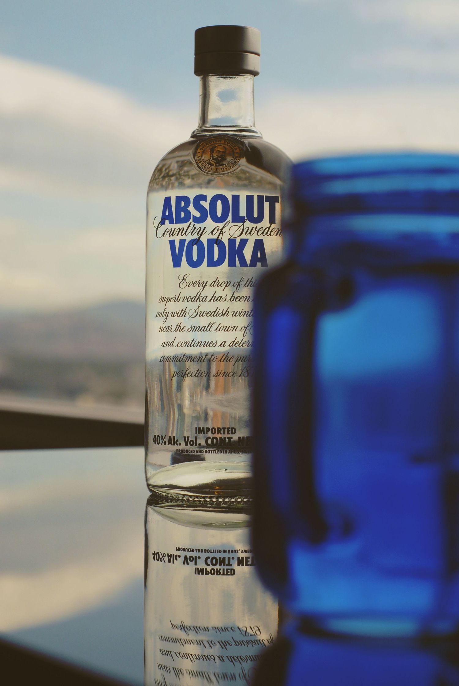 A glass Absolut vodka bottle photographed at different angles against a blurred background with blue tones.