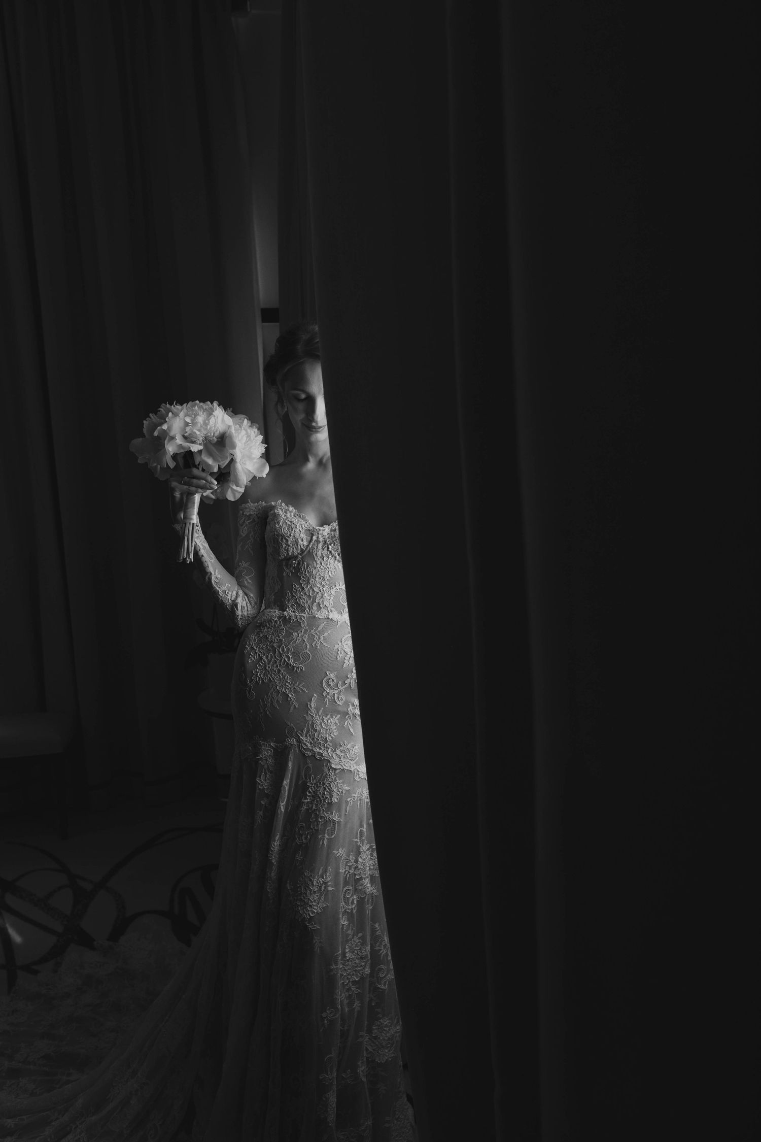 Artistic black and white portrait of a wedding dress and bouquet in dramatic shadows.