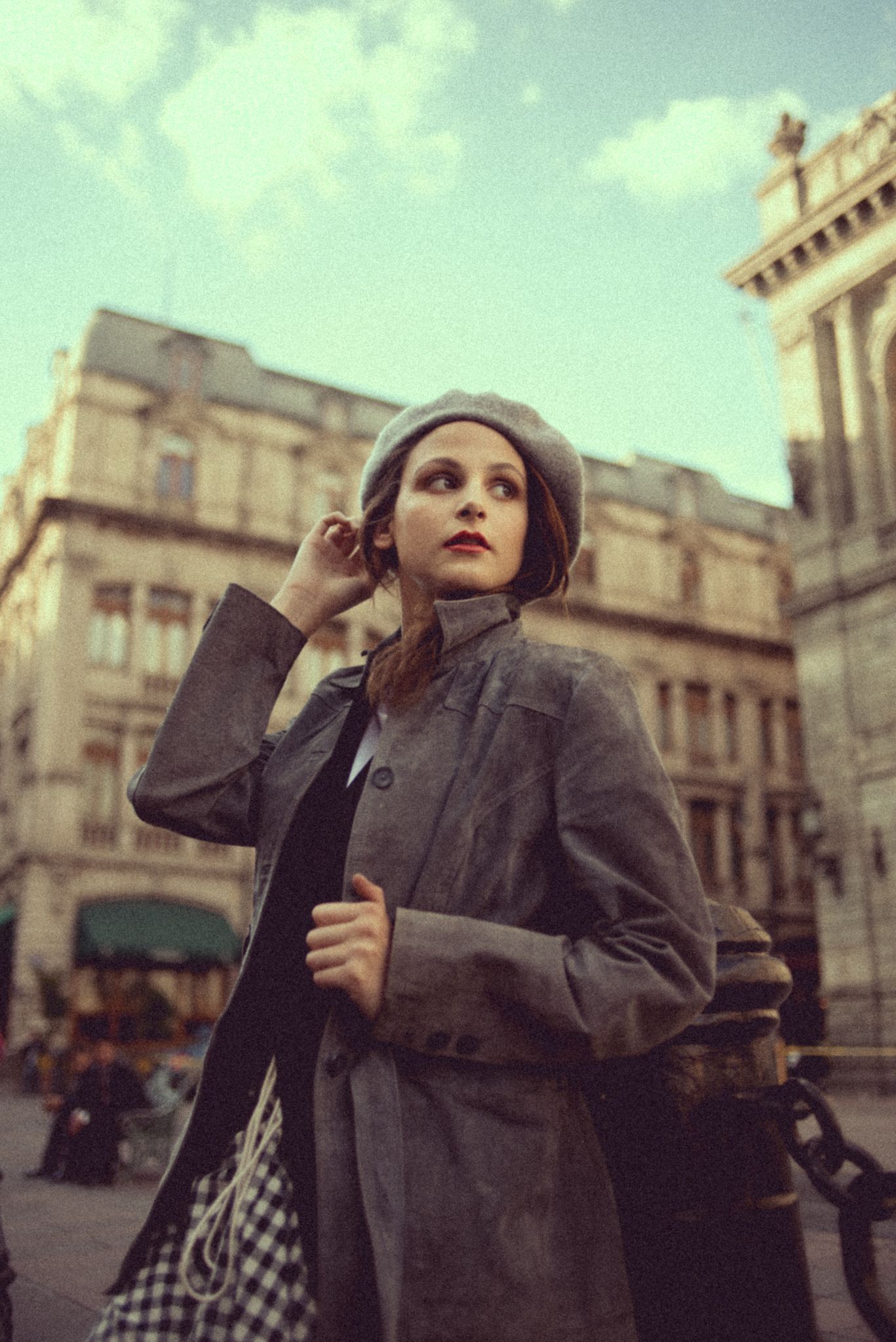 Retro fashion photography featuring grey coat and beret against historic building facade.