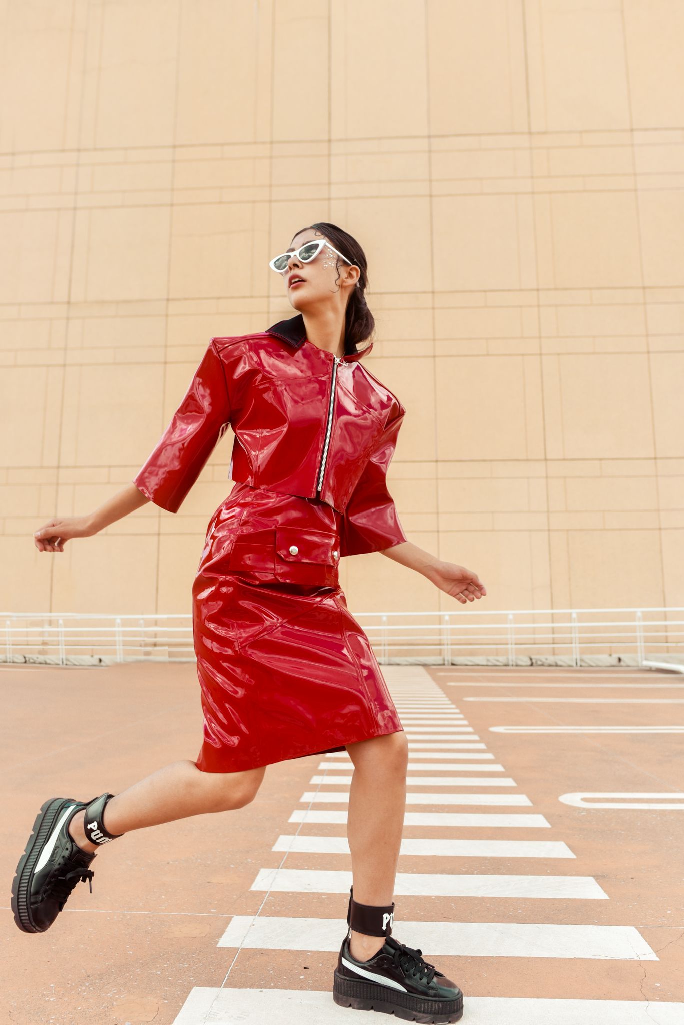Dynamic shot of woman in red vinyl dress jumping on crosswalk.
