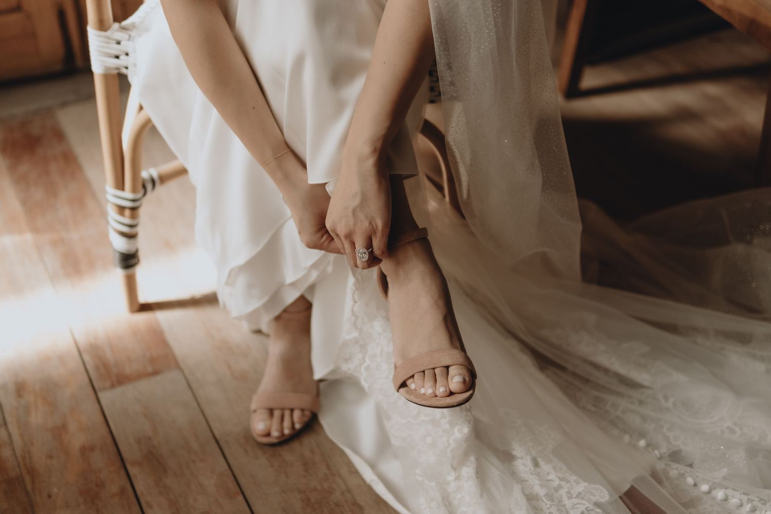 Close-up of bride adjusting her heeled sandals while sitting in her wedding dress.