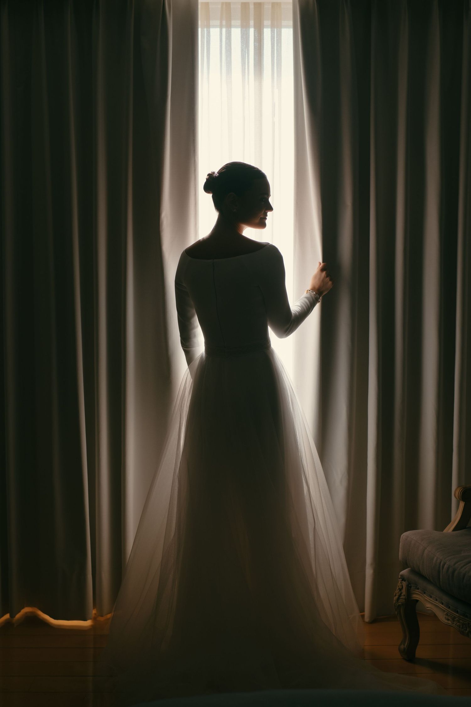 Backlit silhouette of a person in an elegant dress standing between dark curtains.