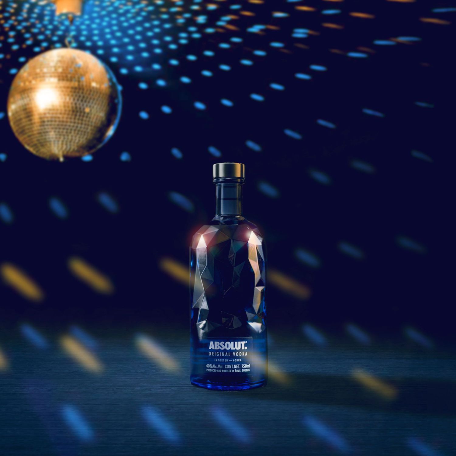 A bottle of blue vodka under a gold disco ball casting reflections on dark background with glowing lights.