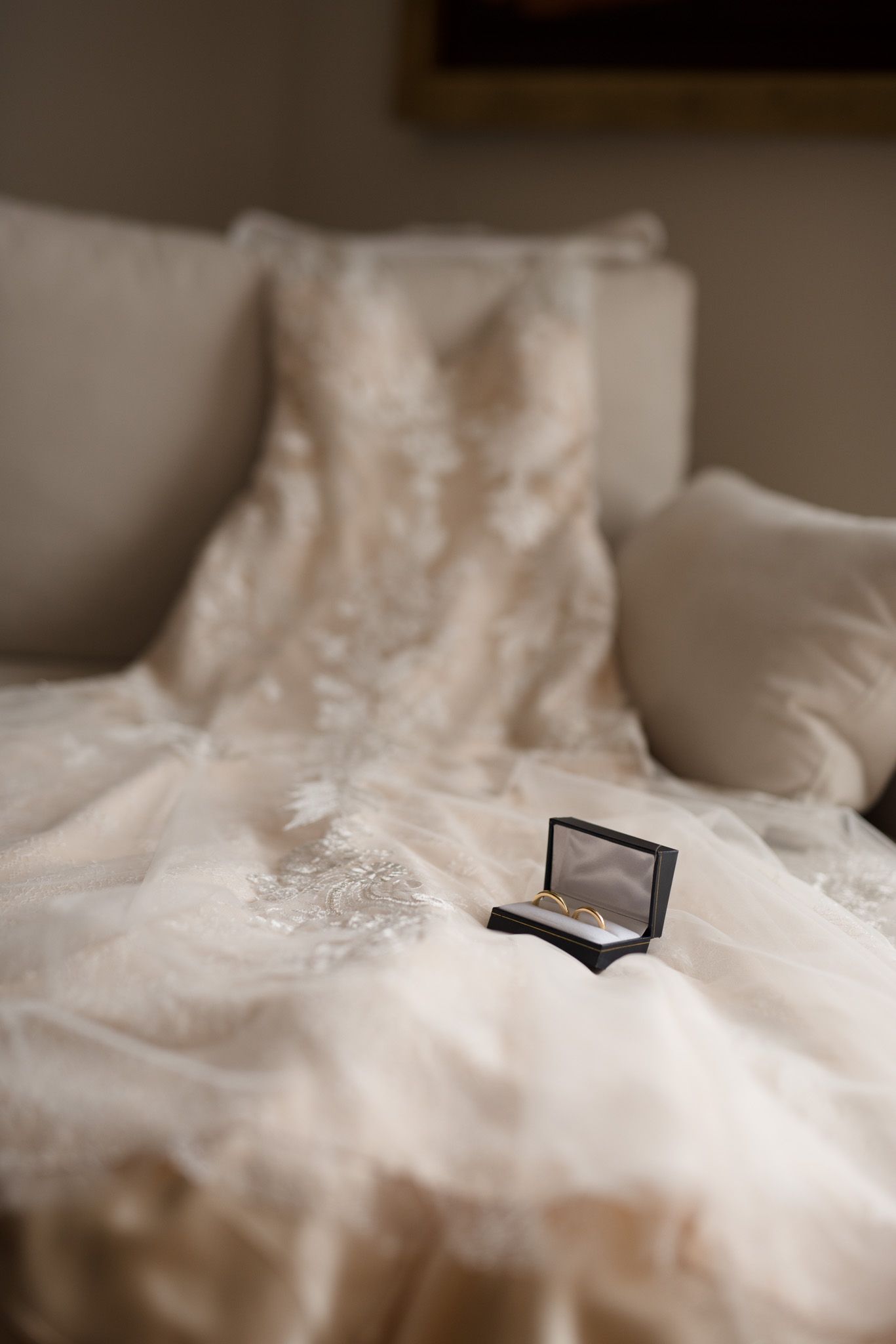 Wedding dress laid out on white couch with small jewelry box displayed on fabric.