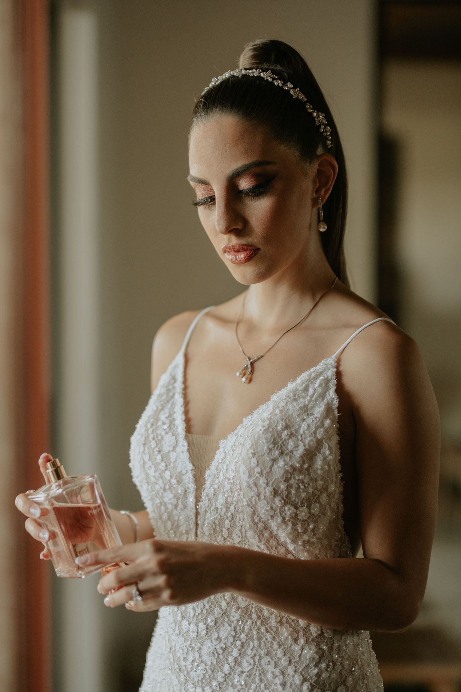 An elegant bridal portrait showing a beaded wedding dress and perfume bottle in soft lighting.