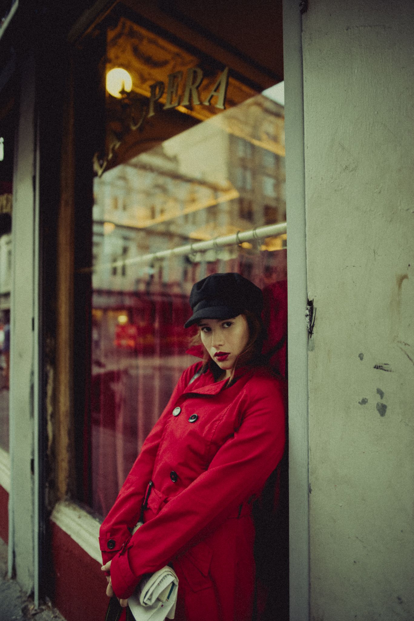 Fashion portrait in bright red coat against urban storefront setting.