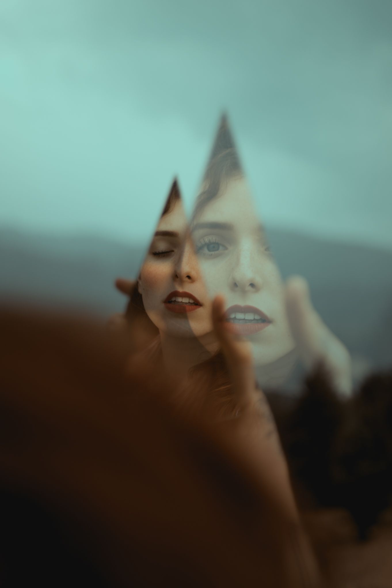 Creative portrait using a mirror shard reflecting against a dreamy teal sky background.