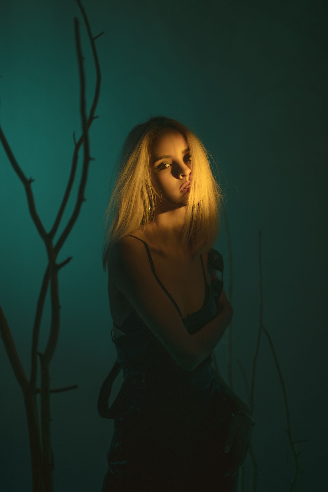 Dramatic portrait in dark teal lighting with bare branches creating moody atmosphere.