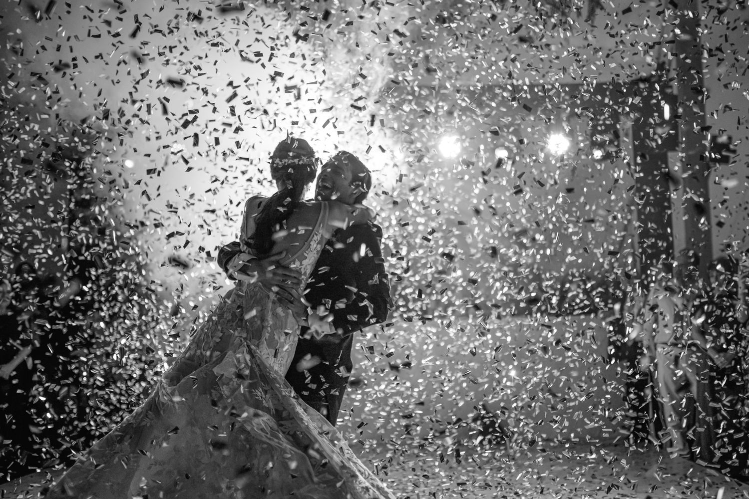 A silhouetted couple dances in a romantic moment surrounded by glittering confetti and backlit by soft lights.