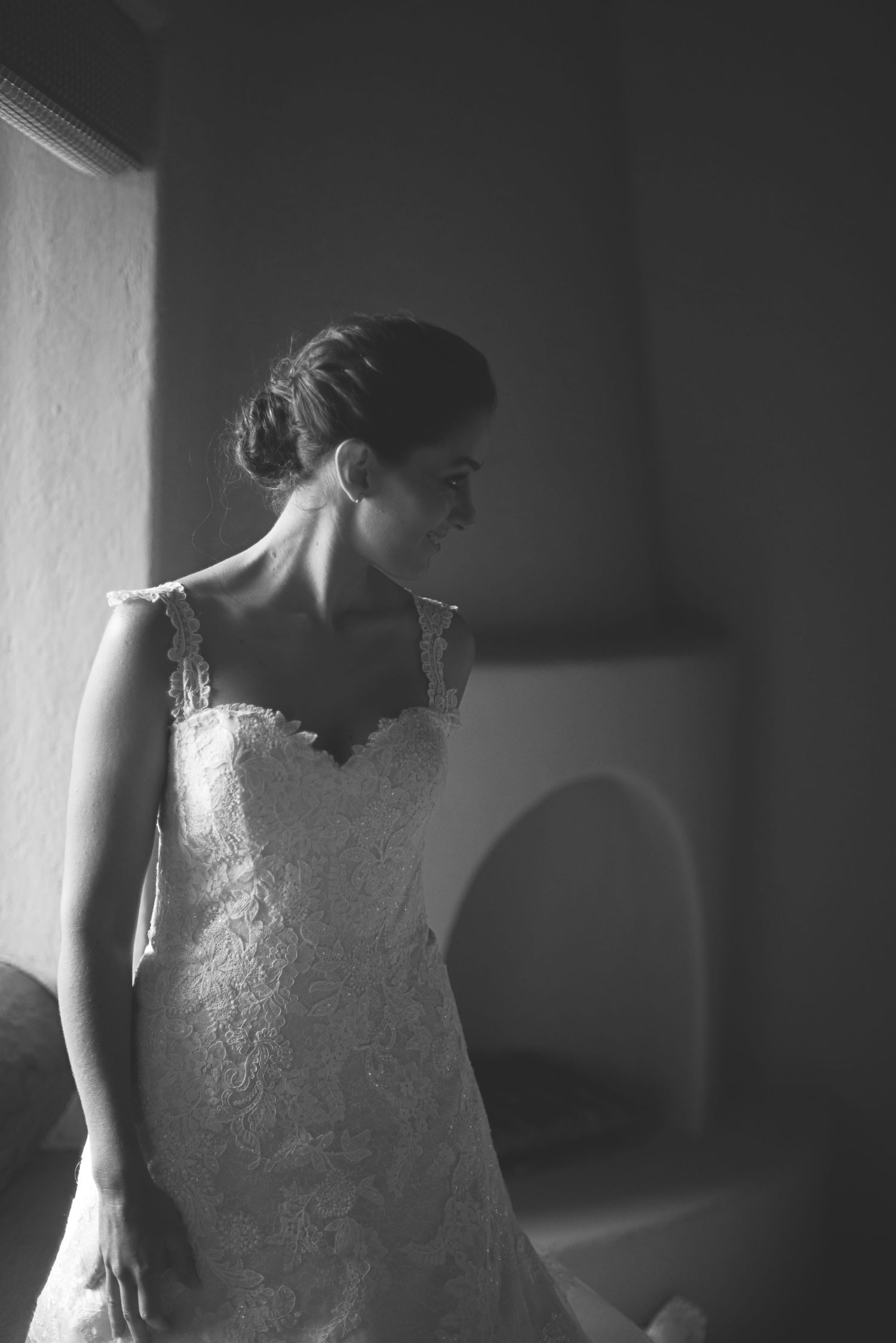 A side-lit black and white portrait of a bride in a delicate lace wedding gown with soft lighting and dramatic shadows.
