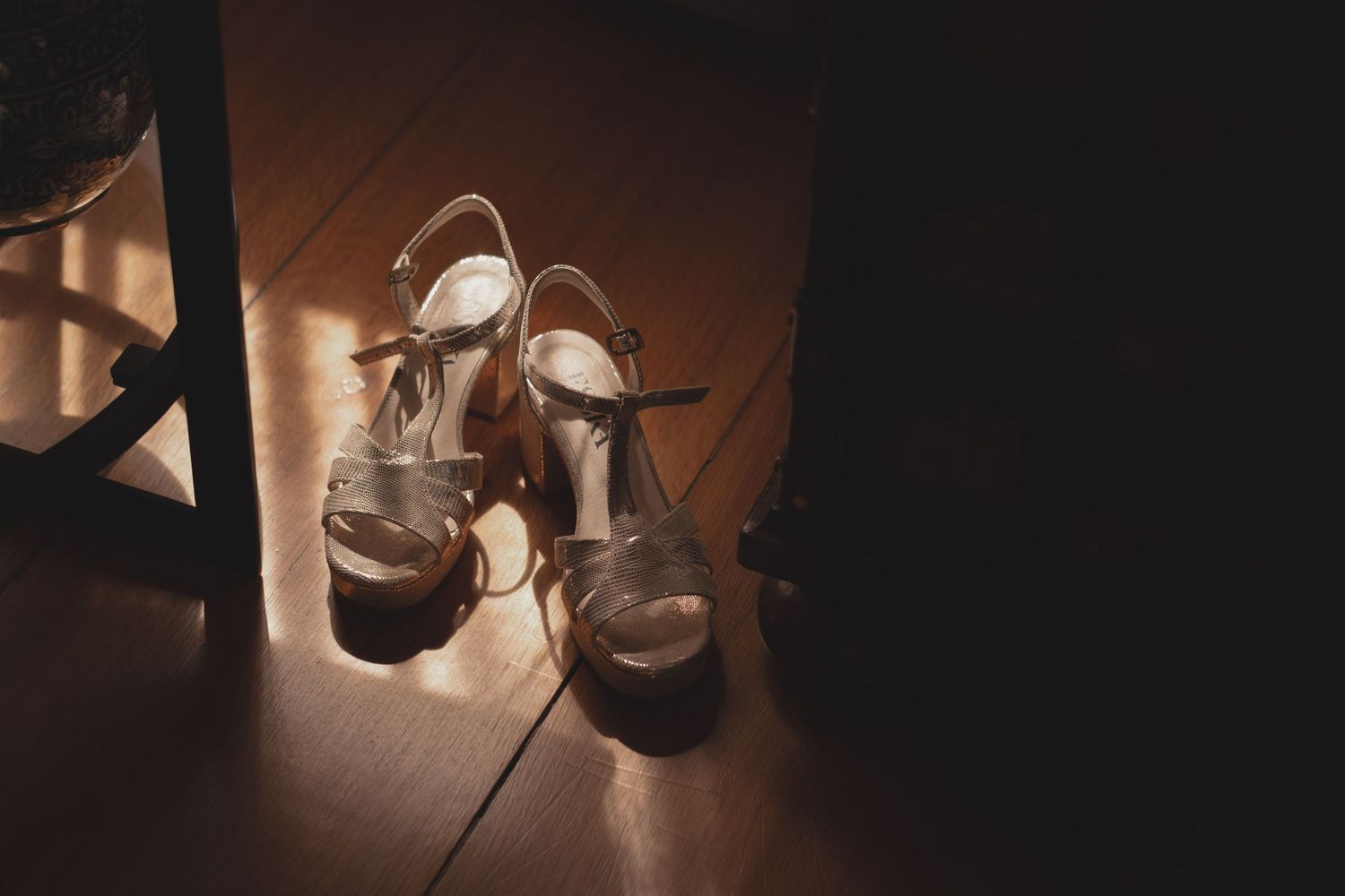 Elegant wedding heels cast dramatic shadows in moody lighting on wooden floor.
