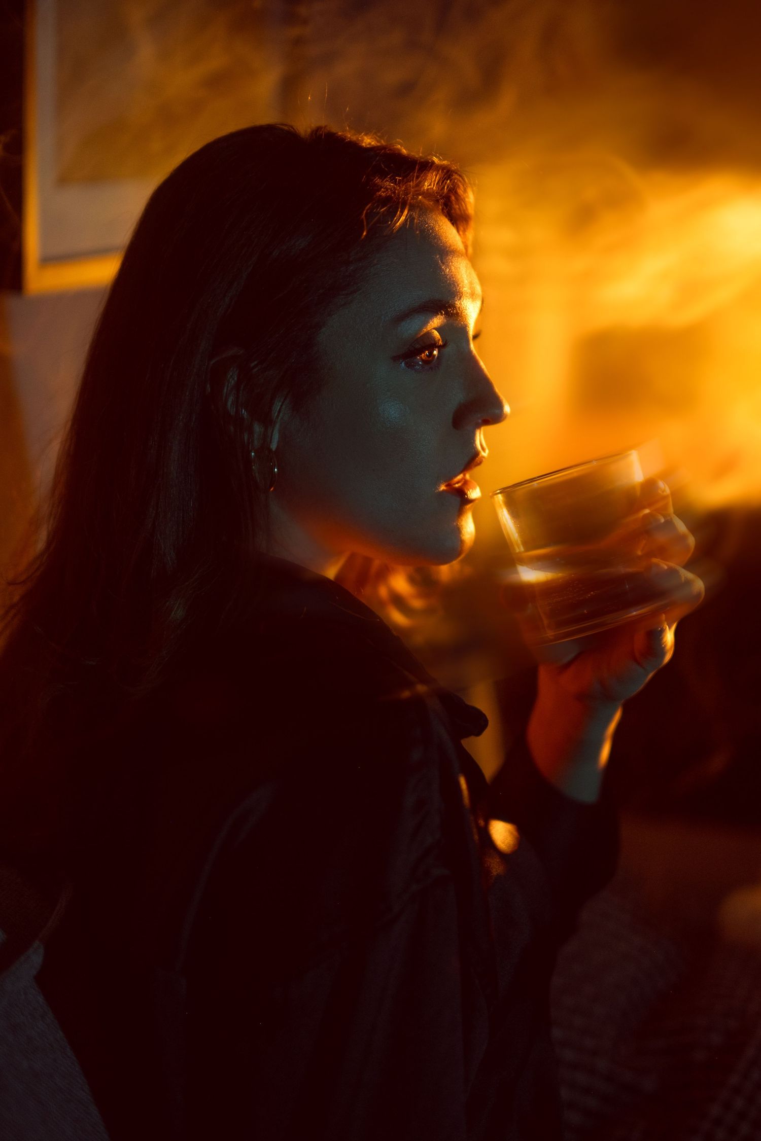 A silhouette holds a glowing drink in moody orange lighting while smoke rises in the atmospheric scene.