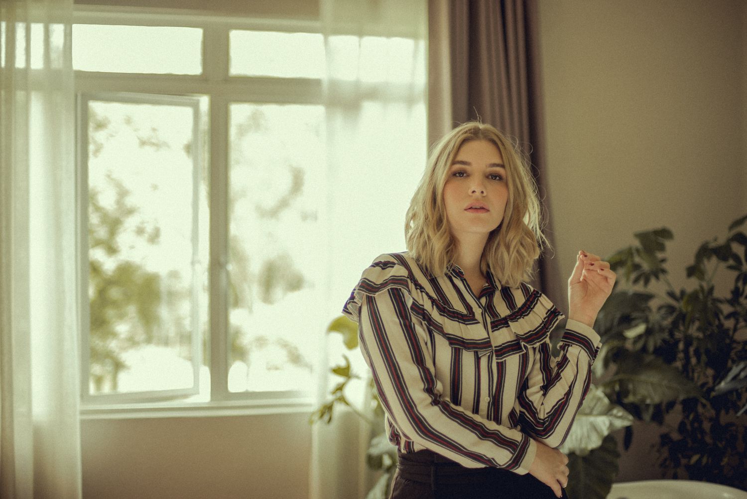 Portrait in striped blouse near window with soft natural lighting and indoor plants.