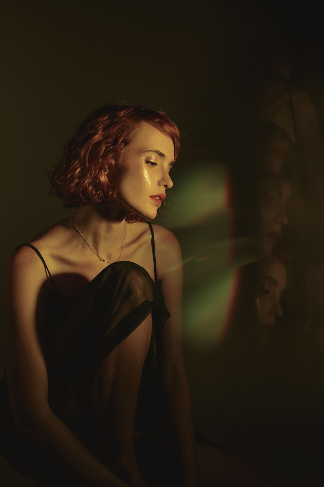 Dramatic low-key portrait in a black dress with moody green lighting and shadows.